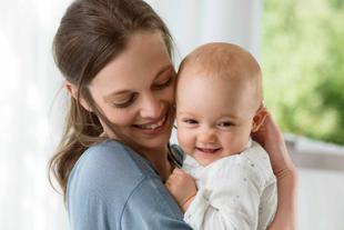 Ein zärtlicher Moment zwischen einer Frau und einem Baby, in dem die Frau das Baby im Arm hält und beide lächeln und einen freudigen Moment teilen.