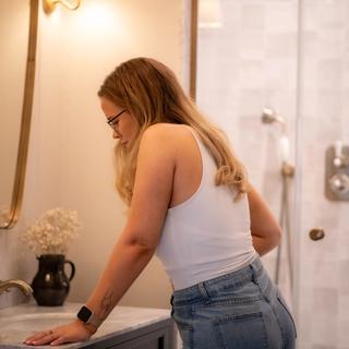 Woman in a bathroom leaning on the sink, looking down thoughtfully, possibly noticing early pregnancy spotting