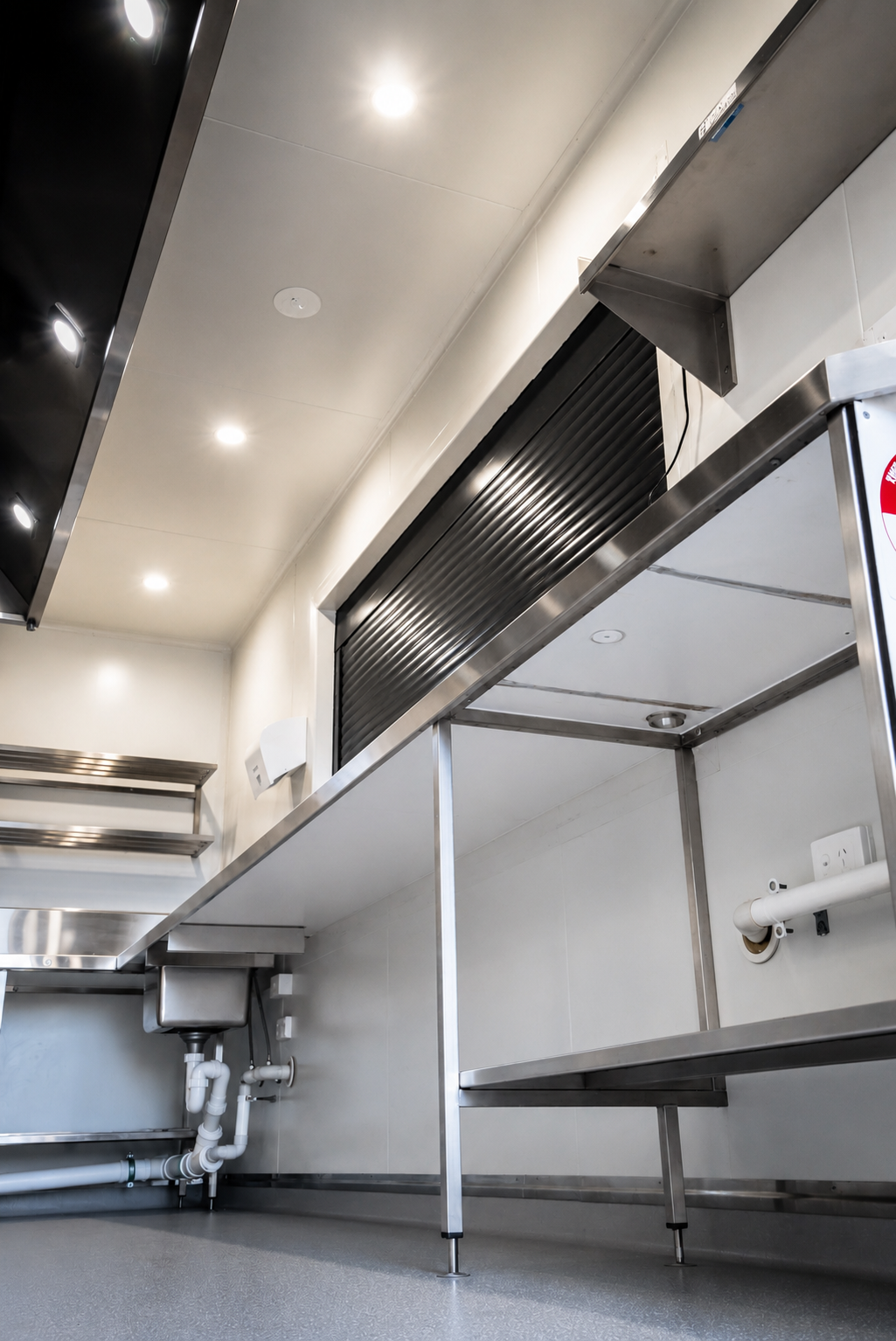 Commercial container kitchen with a stainless steel serving counter, roller shutter servery window, overhead shelving, and durable food-grade finishes