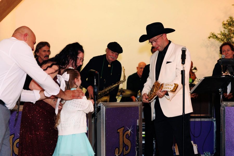 A child is handed a gift in front of the orchestra