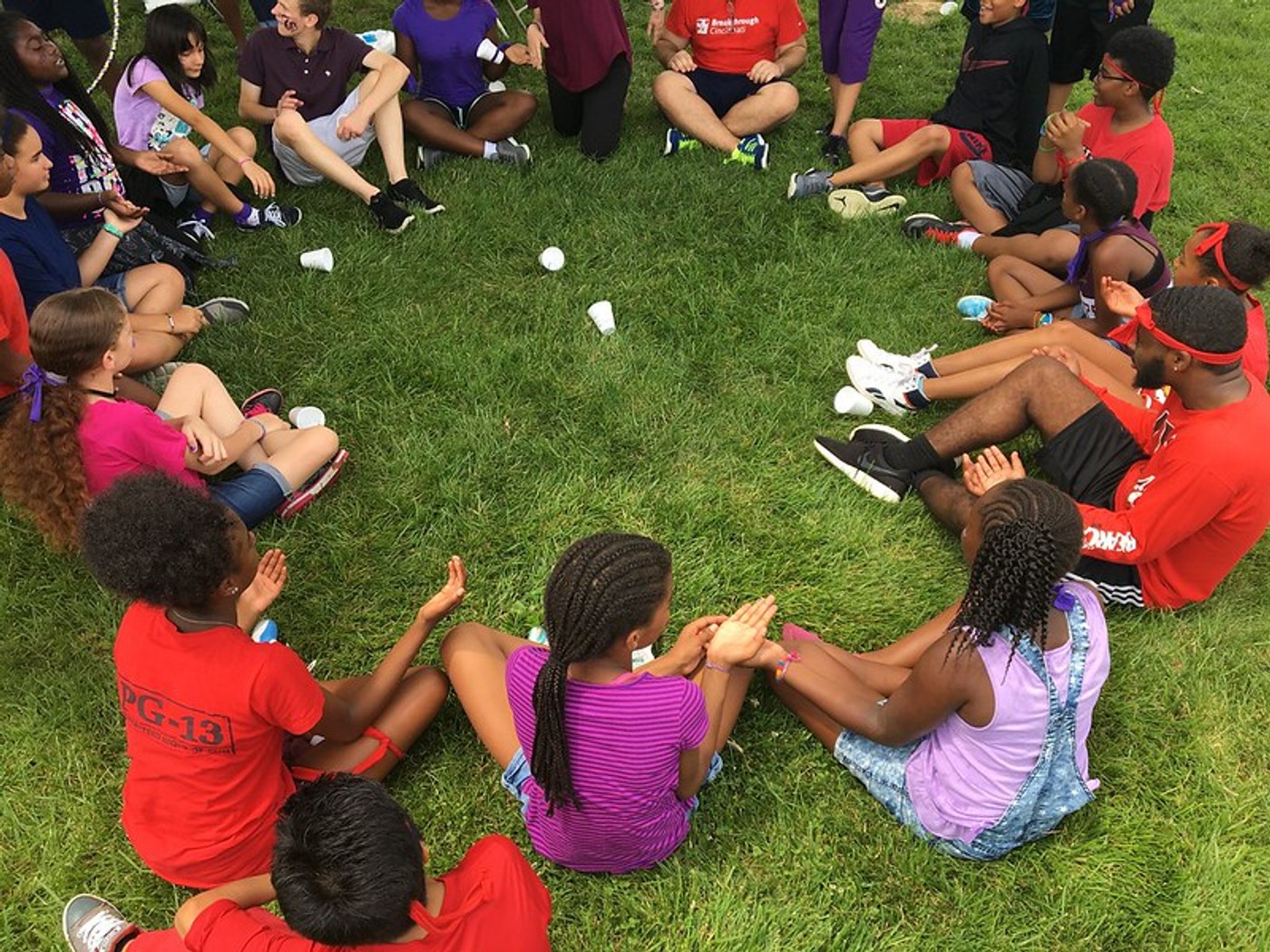 Campers and counselors playing a clapping game in a circle on the grass