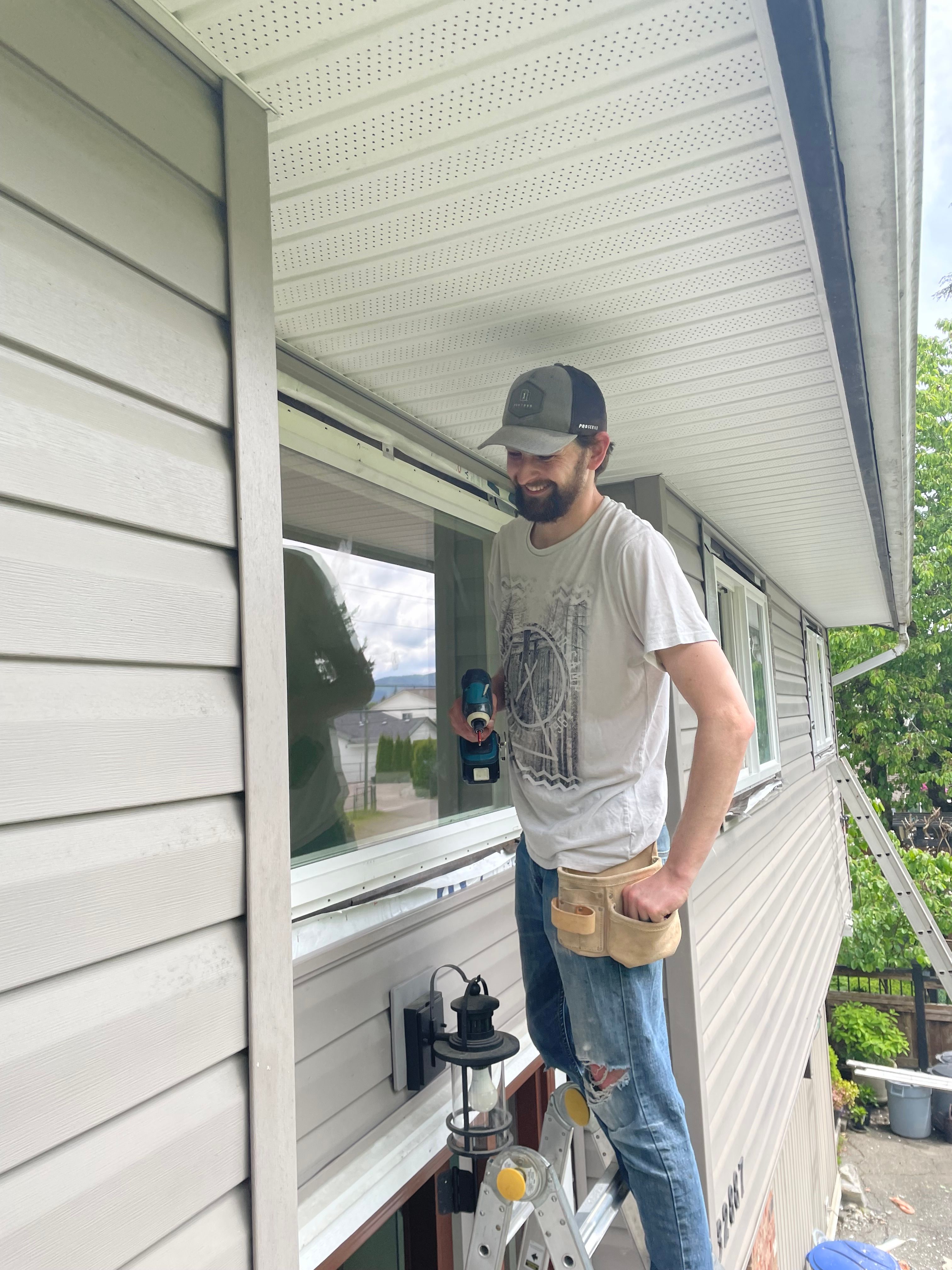 Drew Guthrie installing a second-story dual-pane vinyl window from an extension ladder