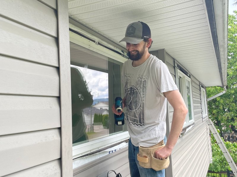 Drew Guthrie installing a second-story dual-pane vinyl window from an extension ladder