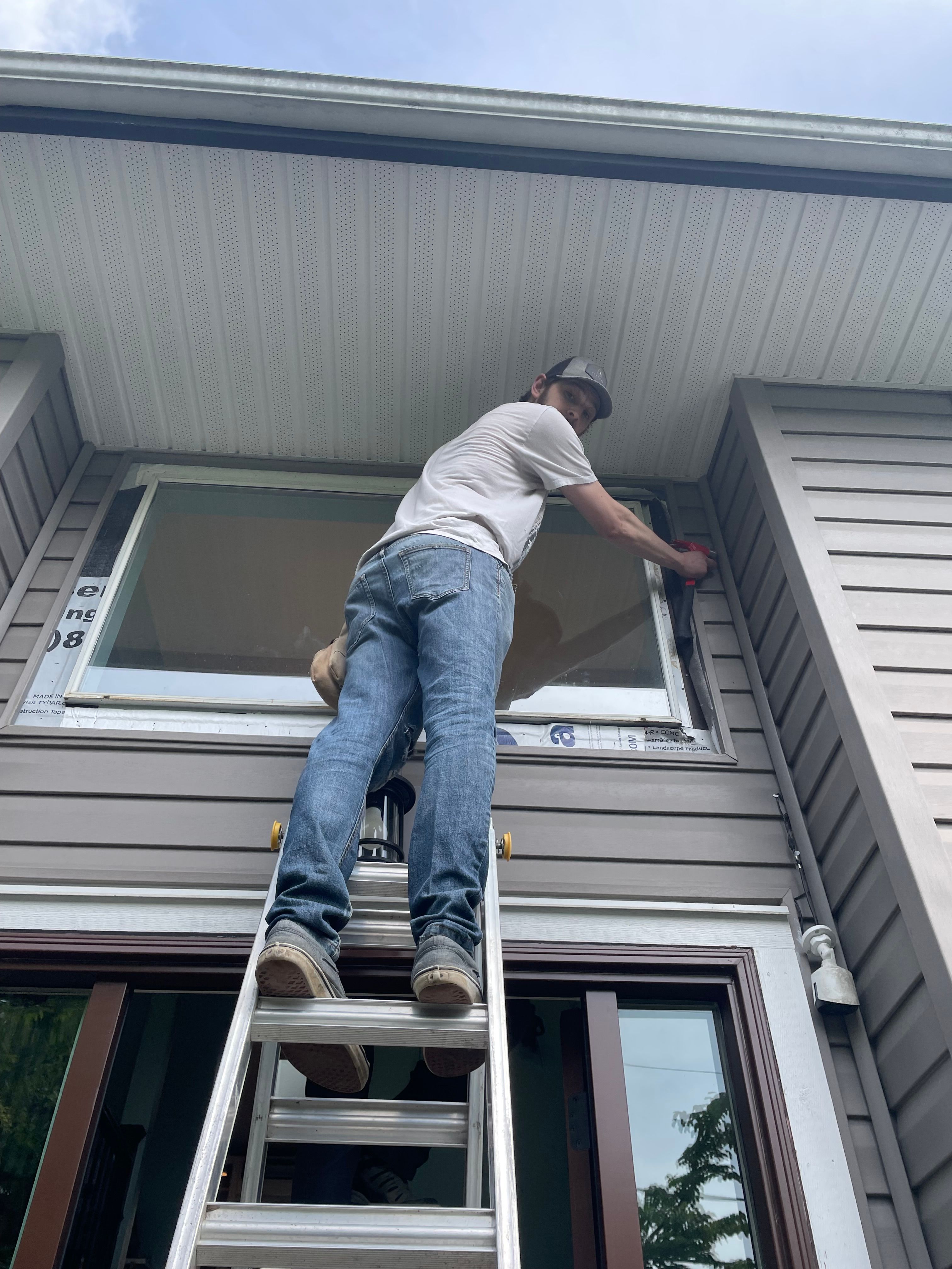 Worker installing a dual-pane vinyl window on the siding side of a two-story home