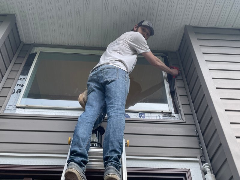 Worker installing a dual-pane vinyl window on the siding side of a two-story home