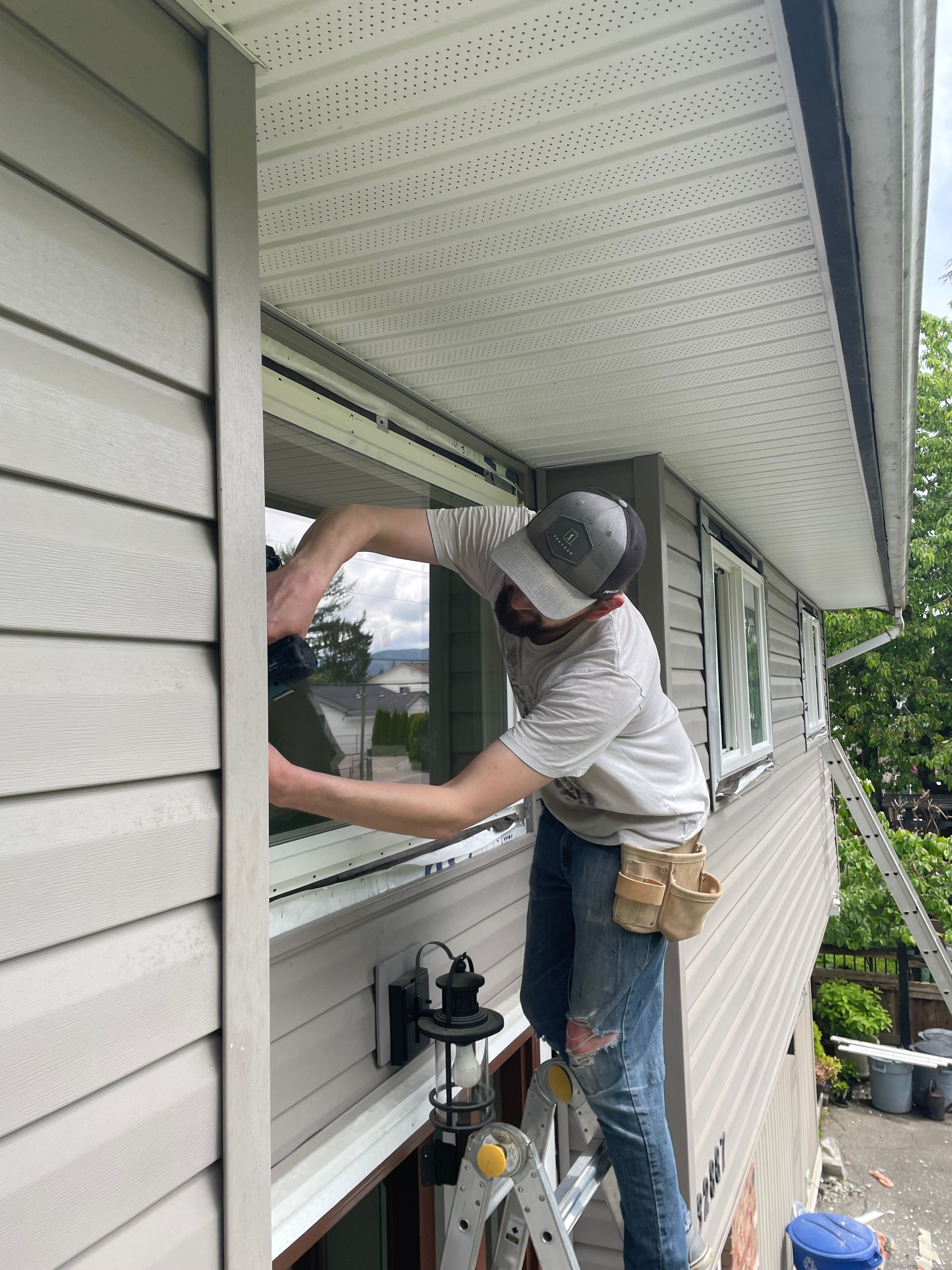 Drew Guthrie setting a dual-pane vinyl window into the rough opening from a ladder