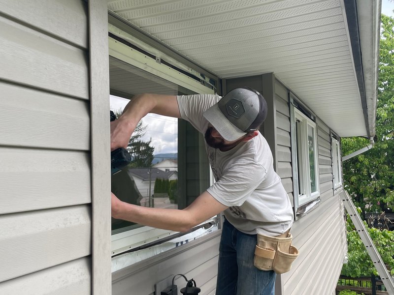 Drew Guthrie setting a dual-pane vinyl window into the rough opening from a ladder