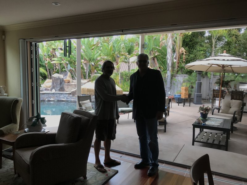 Drew Guthrie shaking hands with a homeowner in front of a multi-panel folding glass door open onto a Wine Country pool and palm-tree backyard