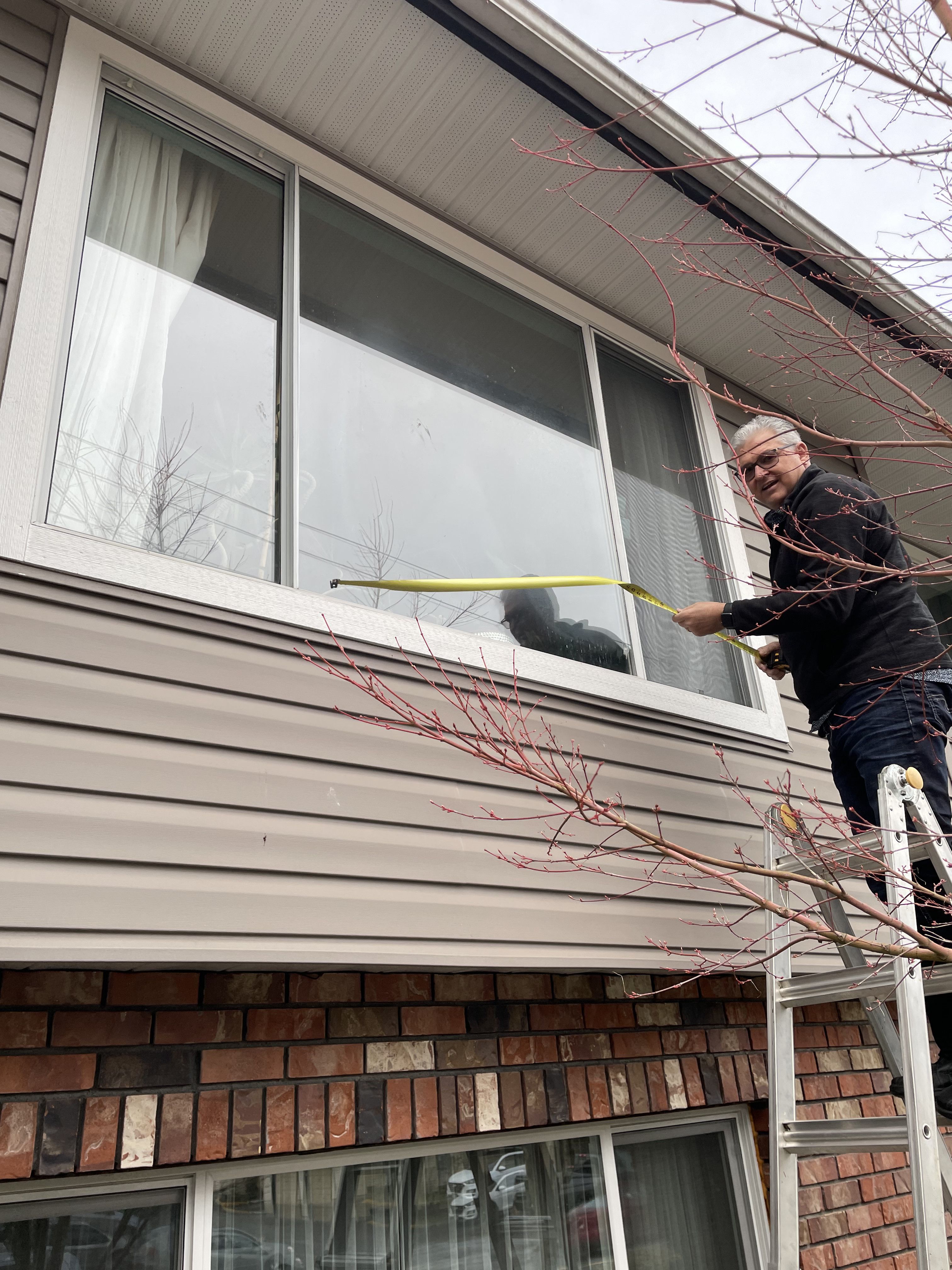 Drew Guthrie taking field measurements for a window replacement quote on a two-story home