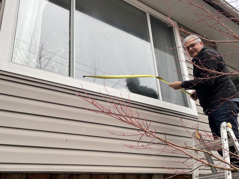 Drew Guthrie taking field measurements for a window replacement quote on a two-story home