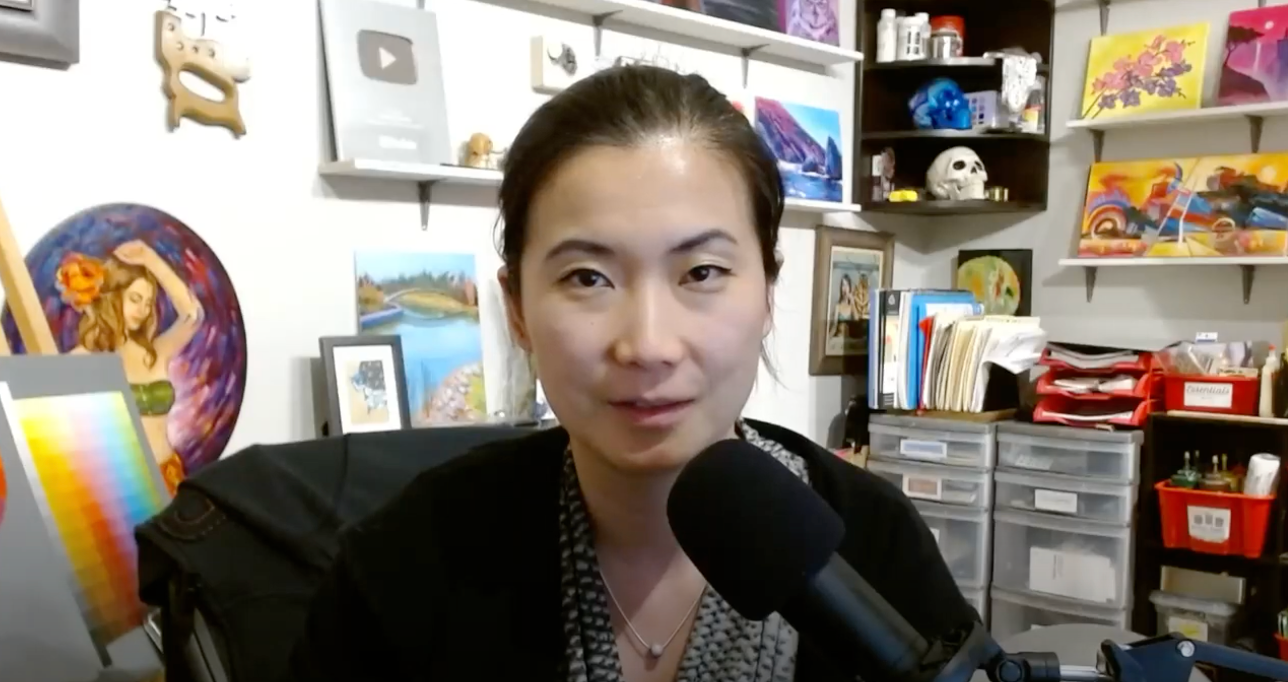 a woman is talking into a microphone in front of a wall with paintings on it