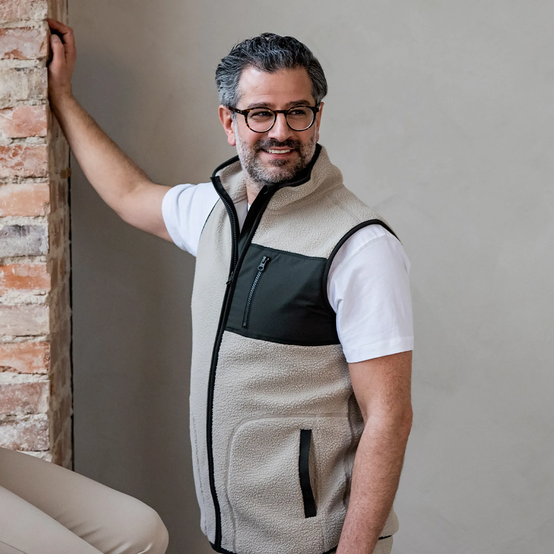 En mjuk, beige fleeceväst med svart zipficka på bröstet och svarta detaljer längs dragkedjorna. Bärs över en vit t-shirt och passar perfekt för lager-på-lager.