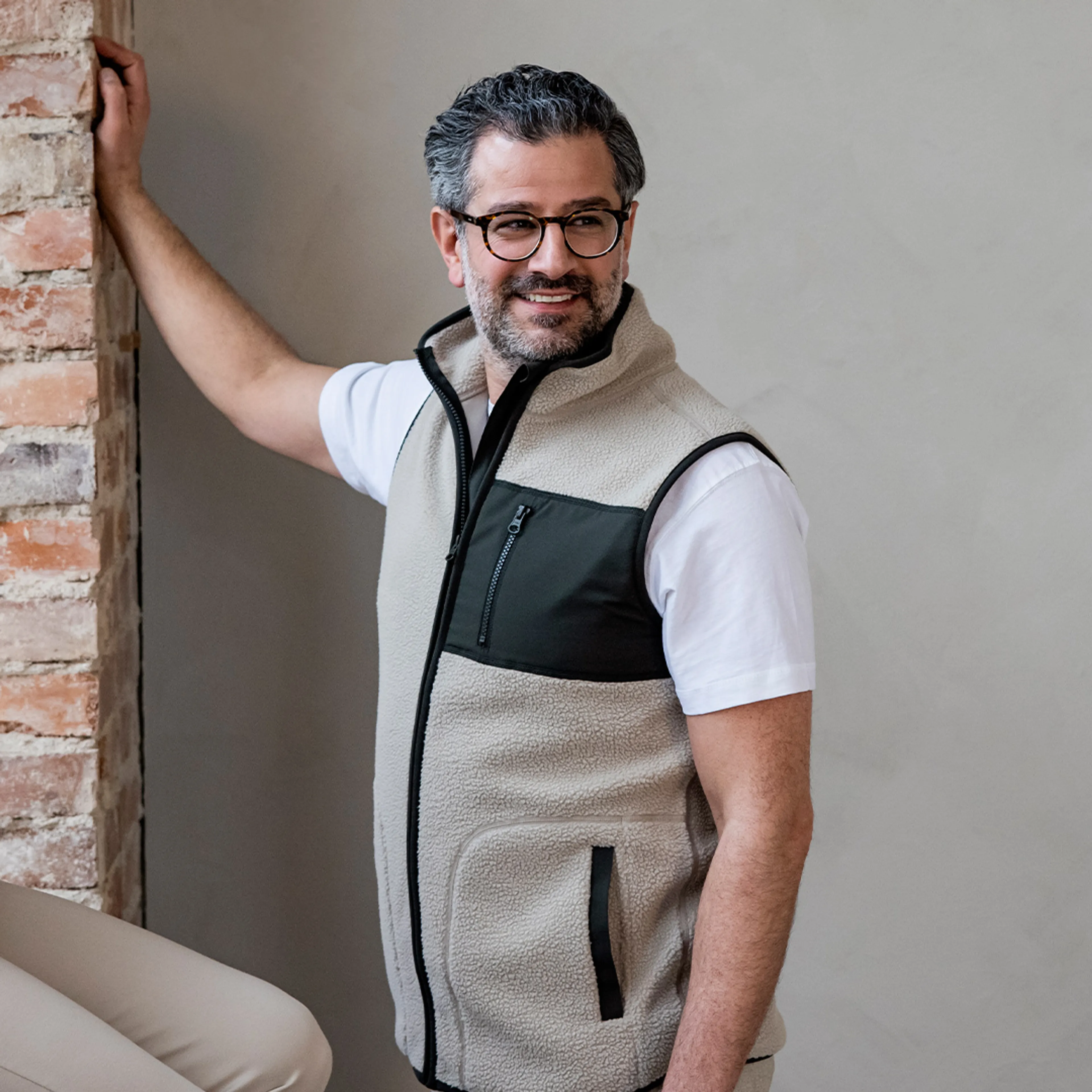 En mjuk, beige fleeceväst med svart zipficka på bröstet och svarta detaljer längs dragkedjorna. Bärs över en vit t-shirt och passar perfekt för lager-på-lager.