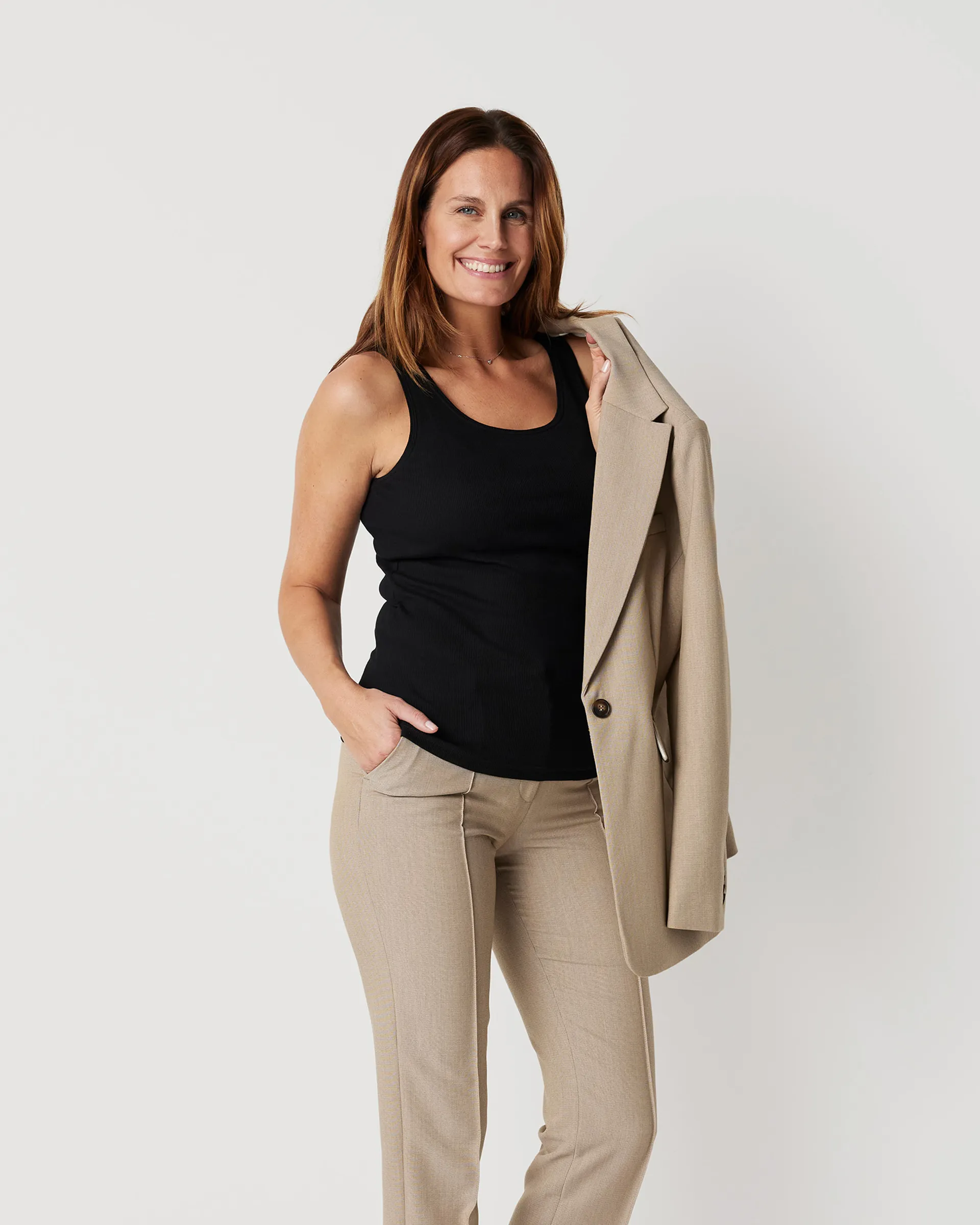 Svart ribbad topp med breda axelband, i en mjuk och följsam passform. Modellen bär toppen tillsammans med beige byxor och håller en matchande kavaj över armen.
