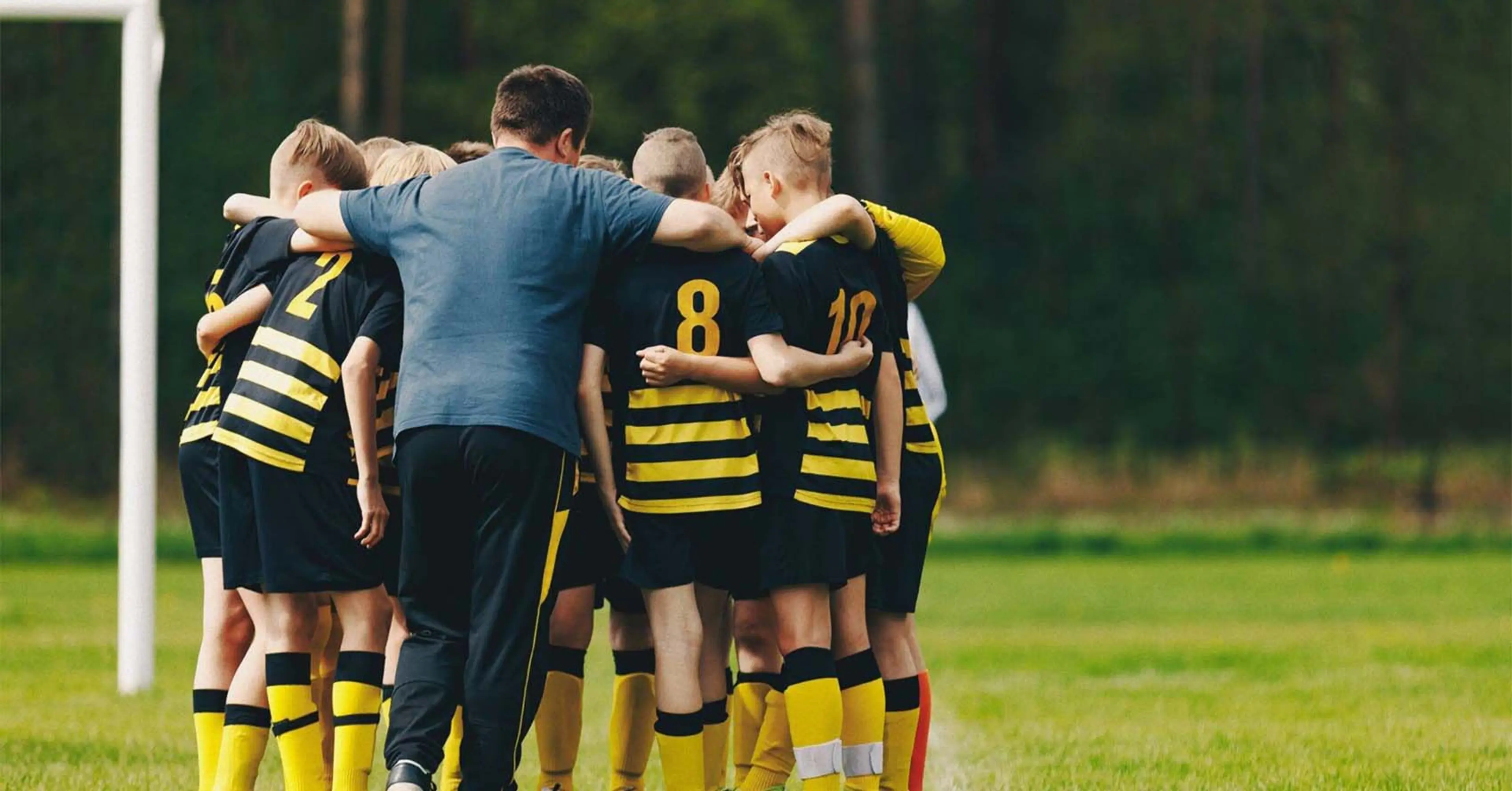 Fotbollslag med svart gula tröjor som står och håller om varandra på fotbollsplan