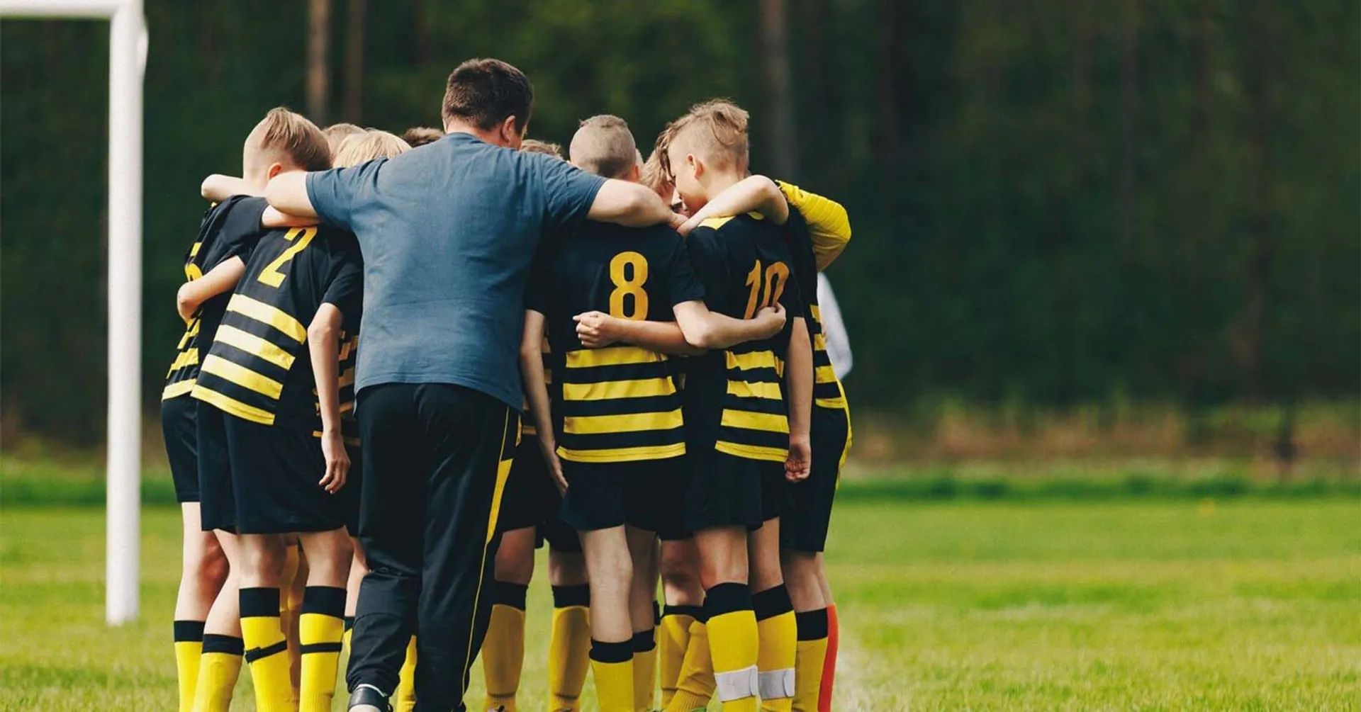 Fotbollslag med svart gula tröjor som står och håller om varandra på fotbollsplan