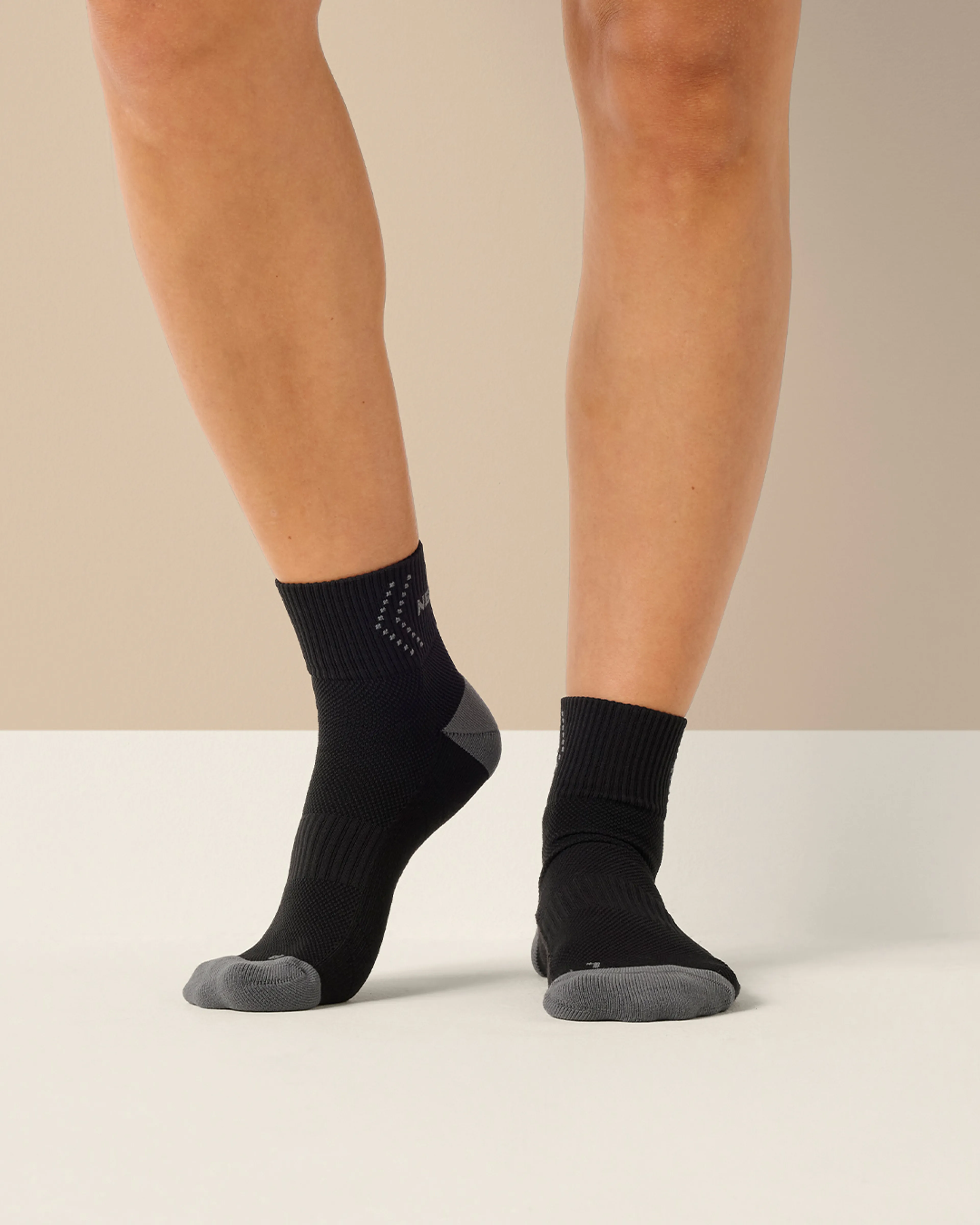 Svarta sportstrumpor med grå förstärkning på tår och häl, designade för extra stöd och komfort. Strumporna sitter bekvämt runt fot och ankel.