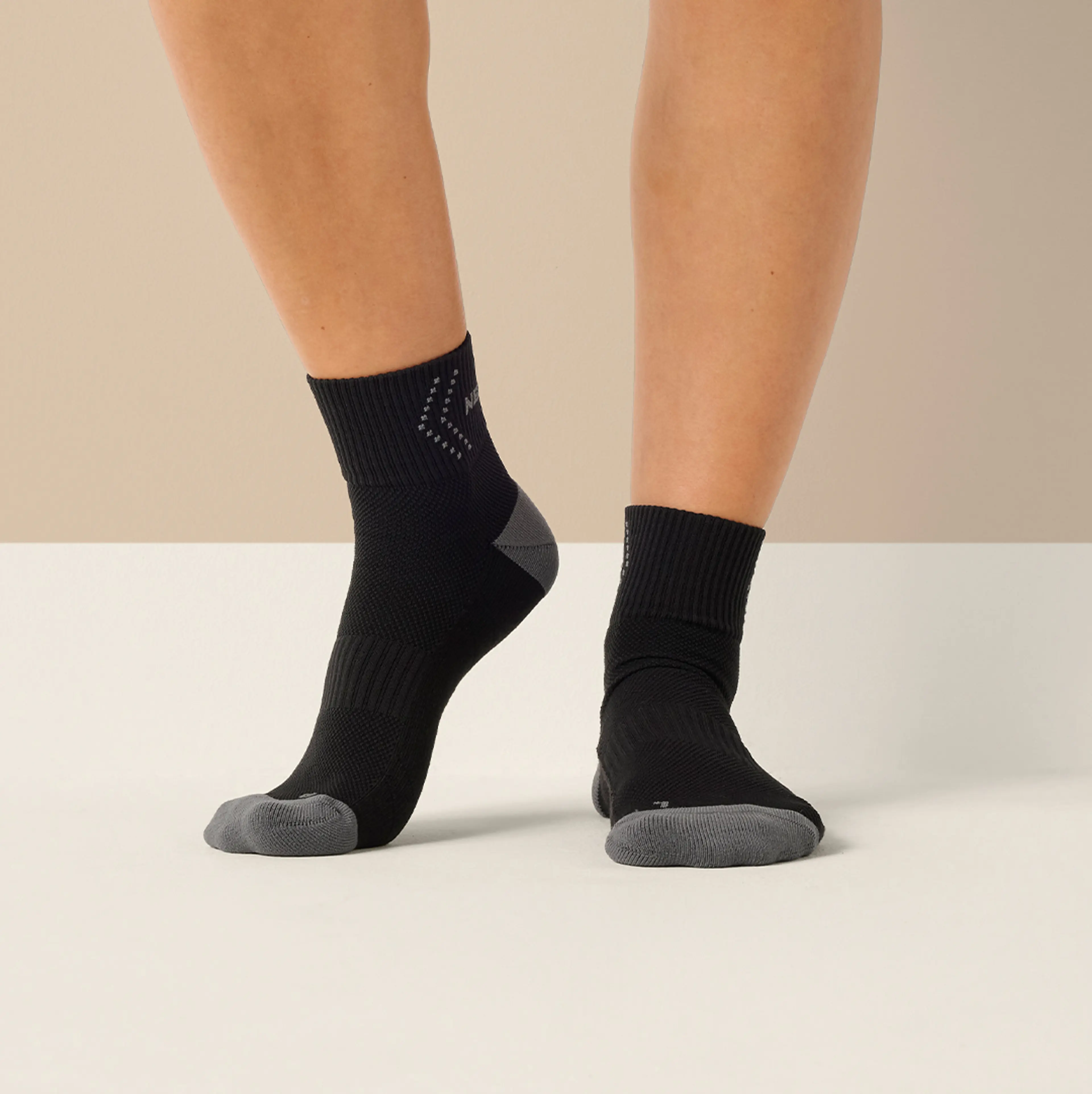 Svarta sportstrumpor med grå förstärkning på tår och häl, designade för extra stöd och komfort. Strumporna sitter bekvämt runt fot och ankel.