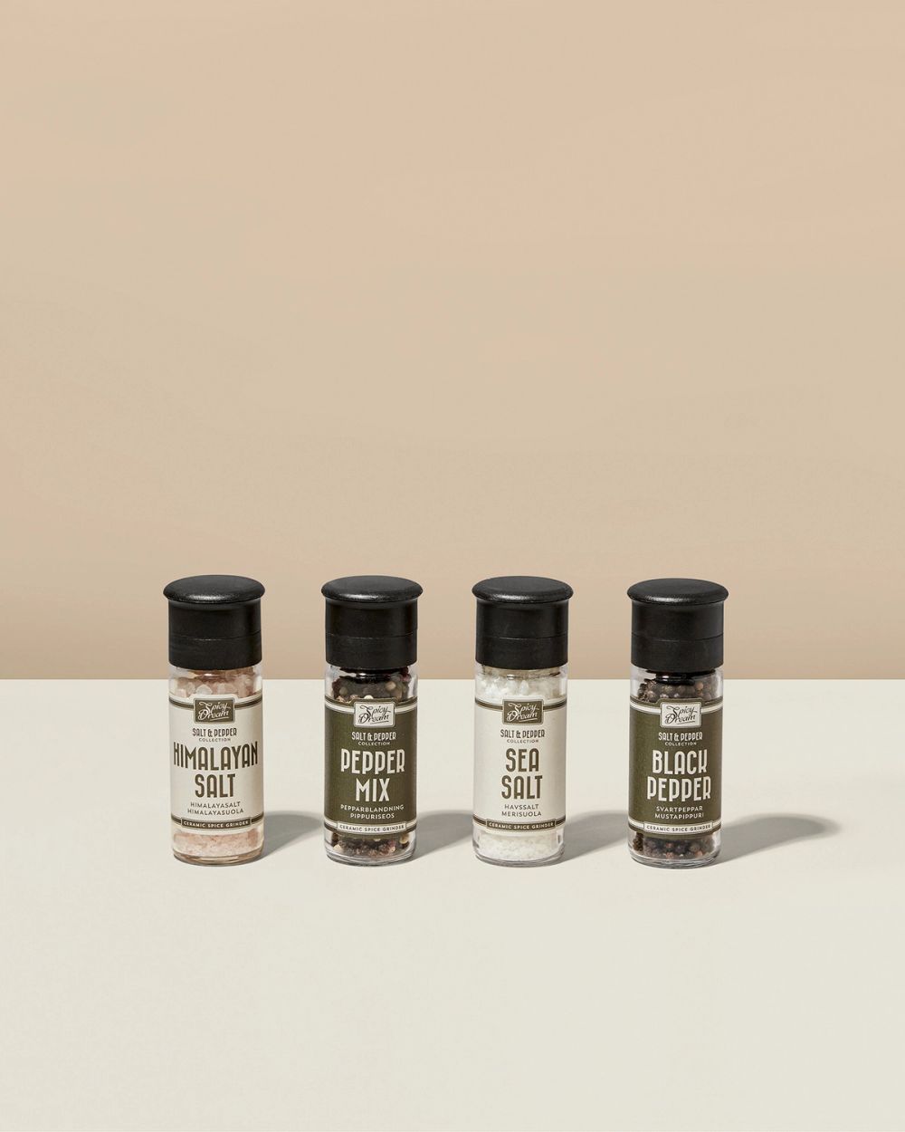 Fyra fina kryddkvarnar i rad med olika innehåll: Himalayasalt, pepparmix, havssalt och svartpeppar. Behändiga storlekar med svart lock mot en beige bakgrund.