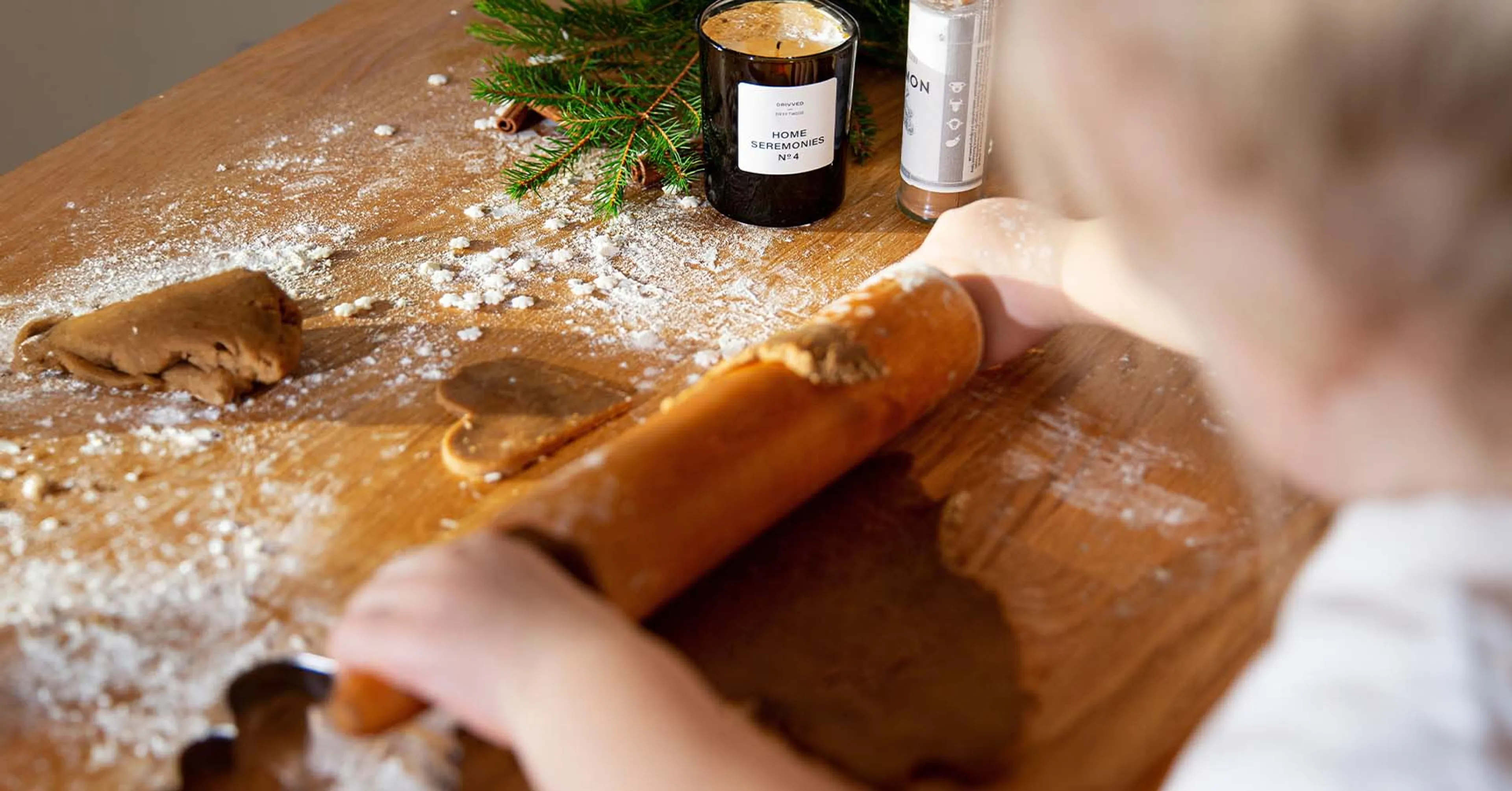 Ett barns armar som kavlar pepparkaksdeg, med ett doftljus och granris i bakgrunden