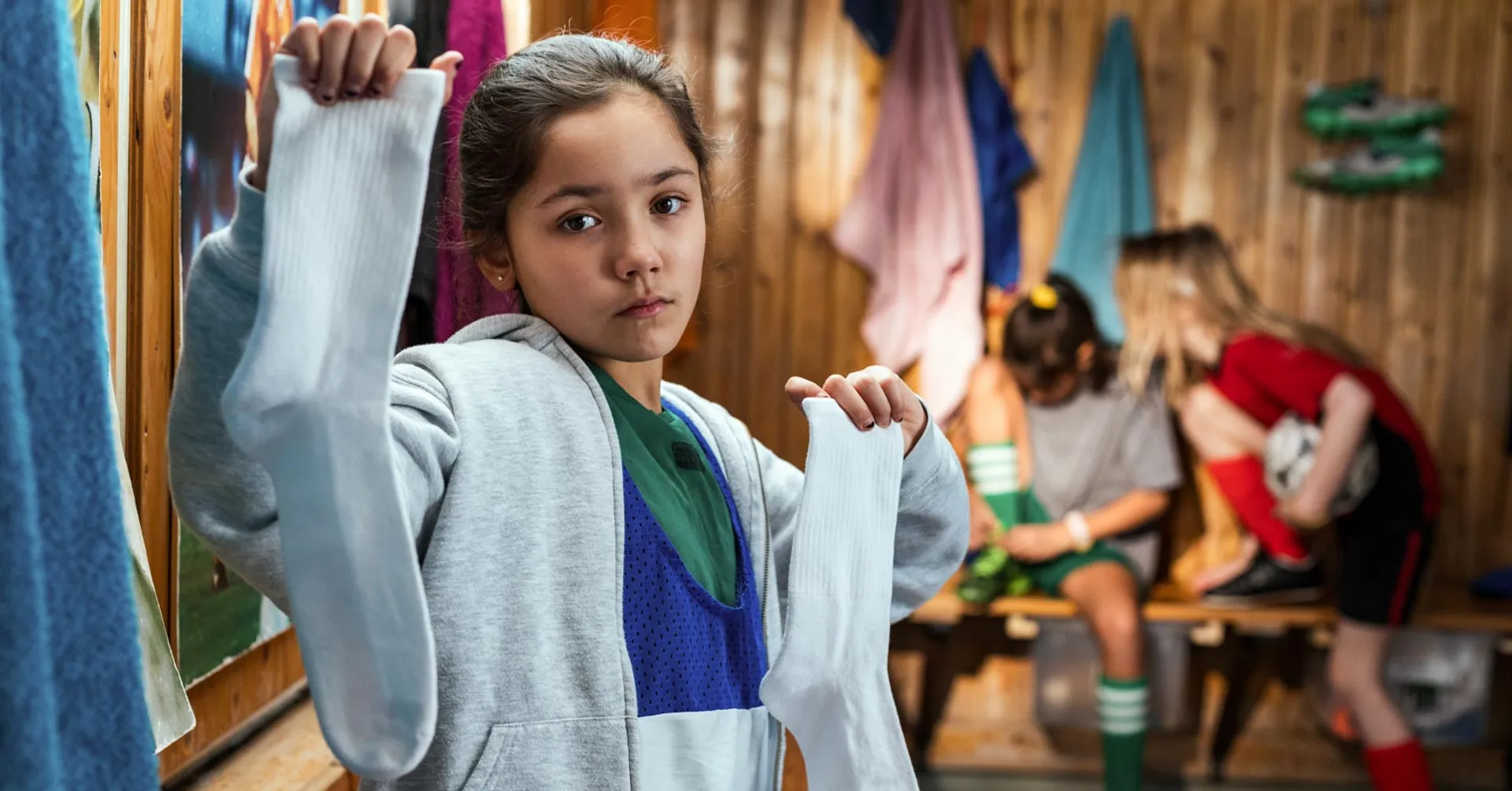 En flicka i ett omklädningsrum som håller upp ett par sportstrumpor för kameran.