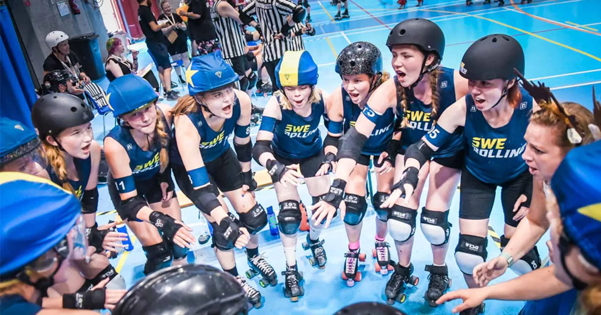Juniorer i rullskridskor med blå och gula hjälmar samlade i en cirkel inför en match i roller derby. De bär skyddsutrustning och matchtröjor med texten "SWE".