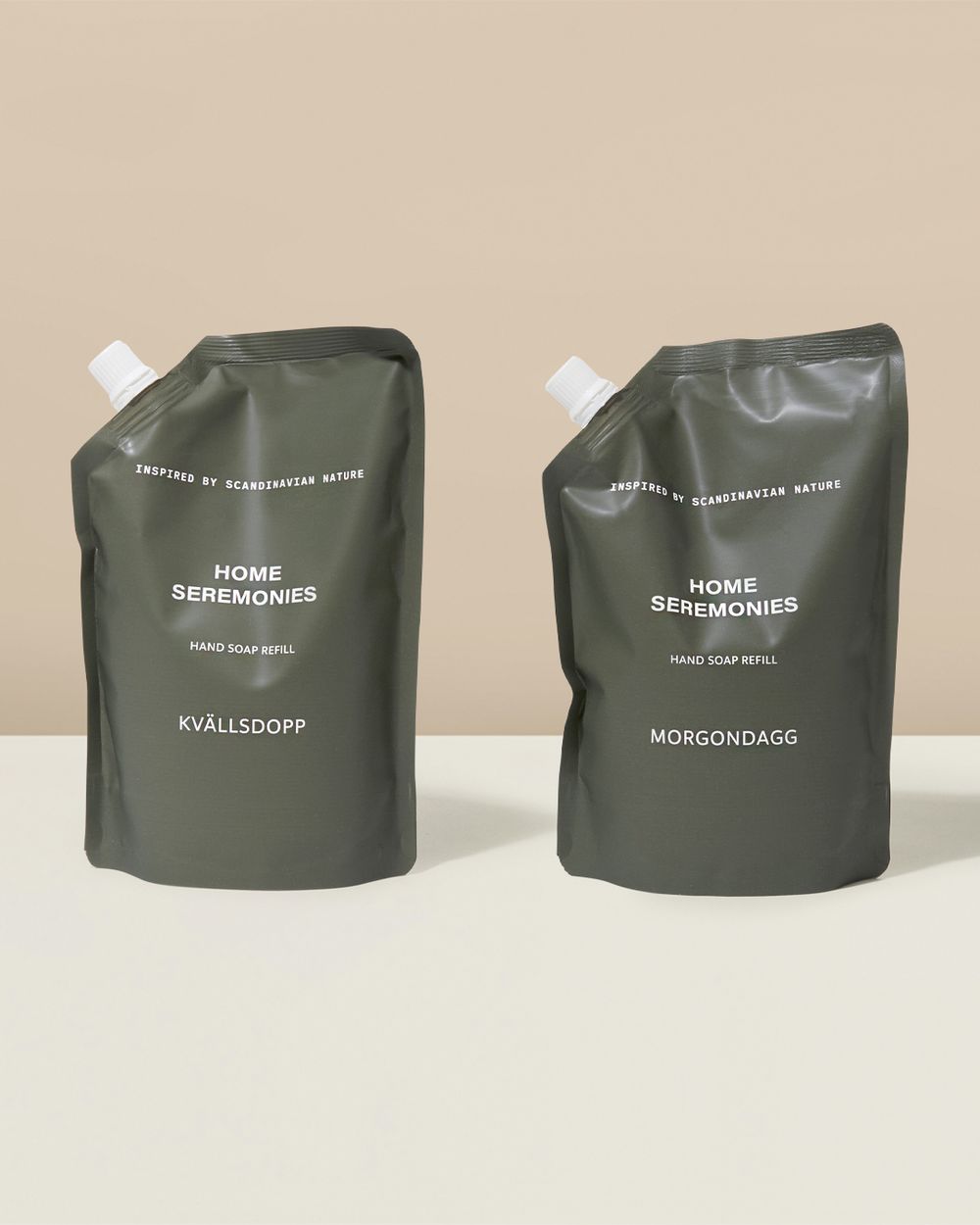 Två påfyllningspåsar för handtvål i mörkgrönt med vit text, märkta "Kvällsdopp" och "Morgondagg". Påsarna har en liten vit kork för enkel användning.