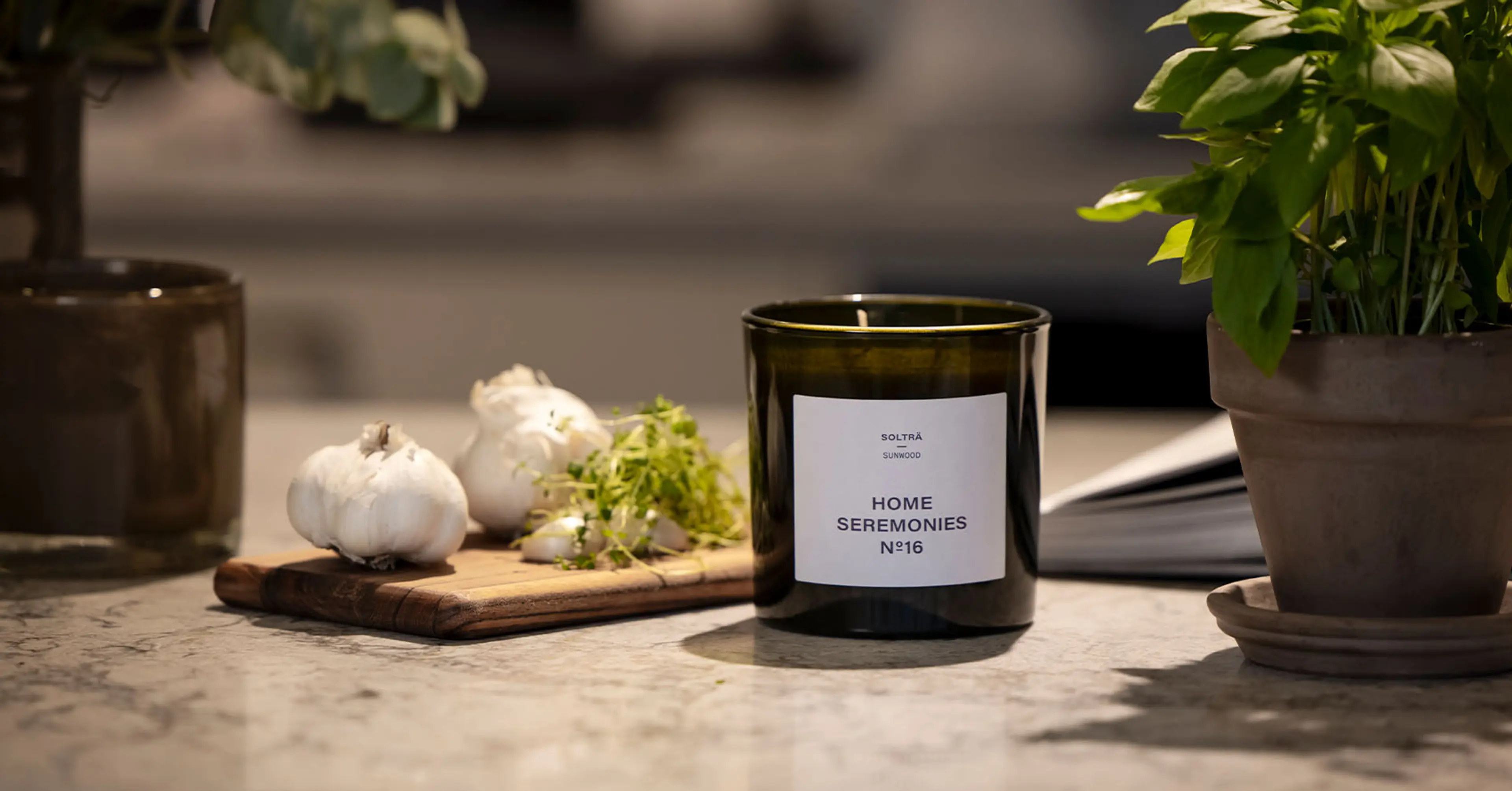 Doftljus står på en köksbänk med vitlök och basilika i bakgrunden