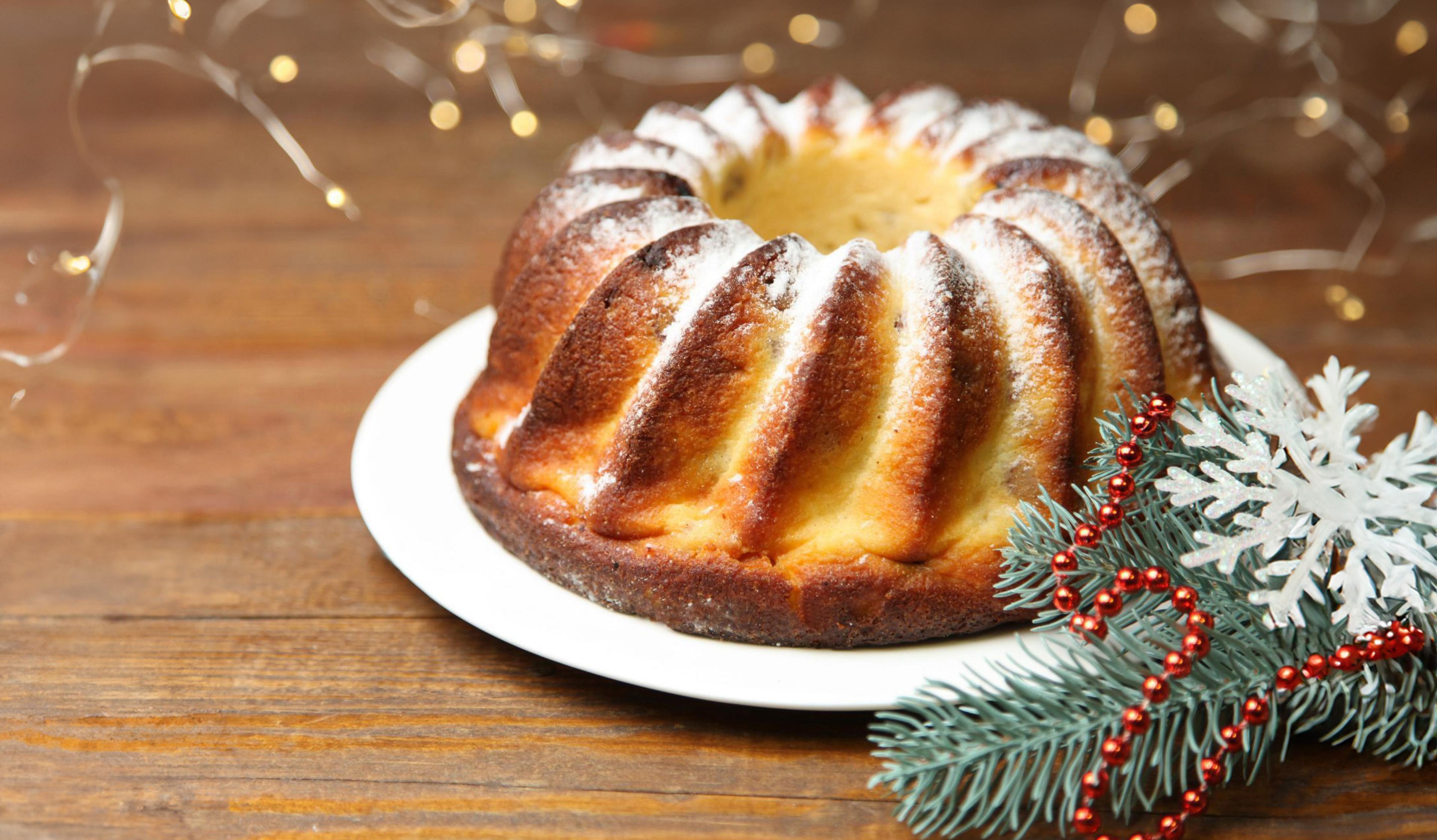 En saftig saffranskaka med en gyllene yta, pudrad med florsocker. Dekorerad med granris, röda kulor och en glittrande snöflinga för en julig känsla.