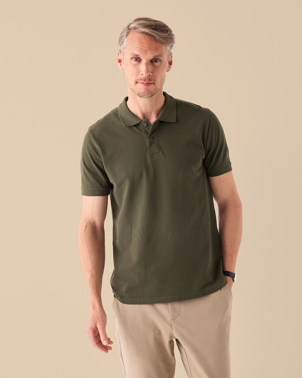 Manlig modell bär en skogsgrön piké t-shirt, sedd framifrån.
