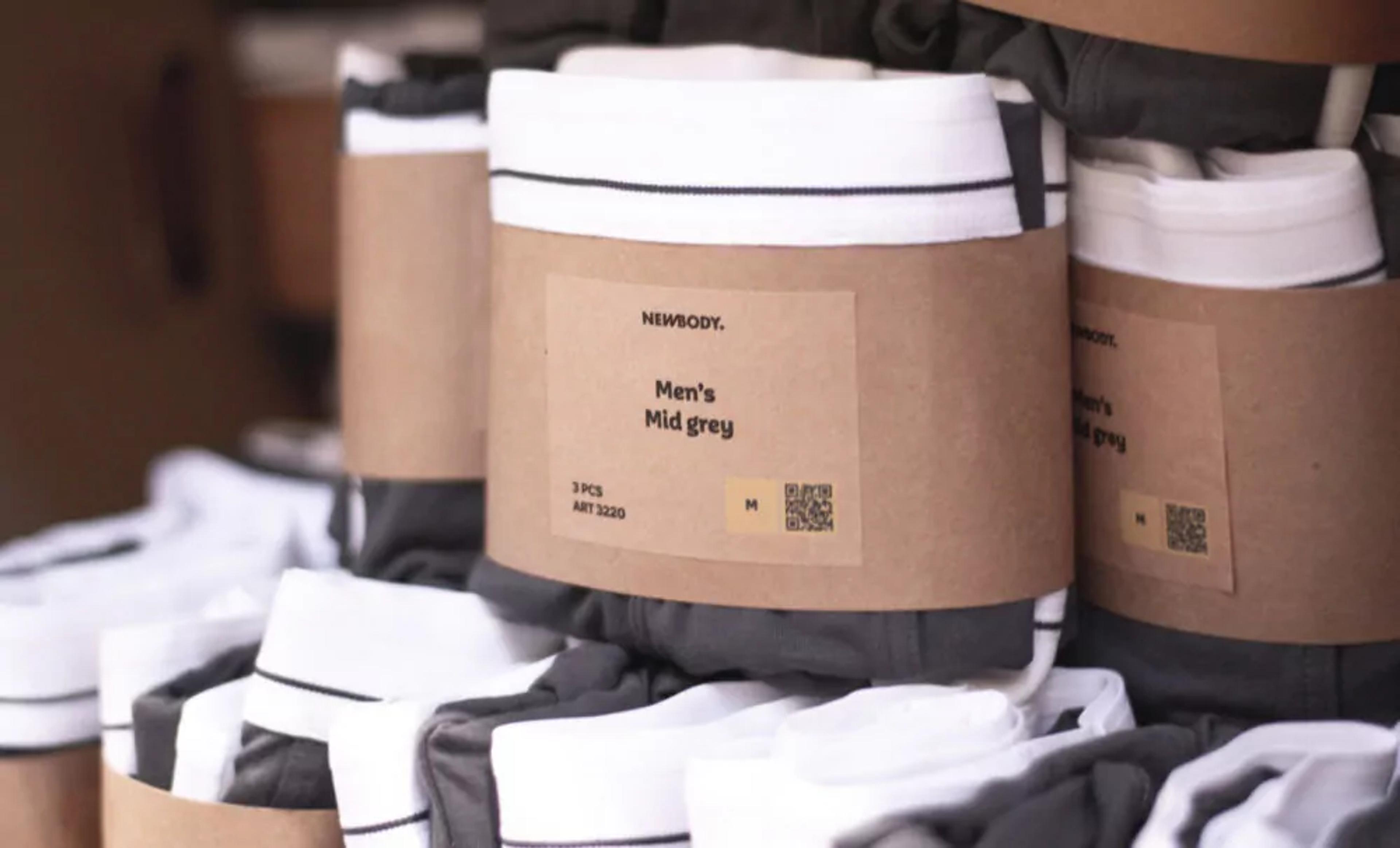 Flera paket med medelgråa och vita herrunderkläder prydligt ihoprullade och försedda med brun pappersetikett. Varje paket innehåller tre plagg i storlek M.
