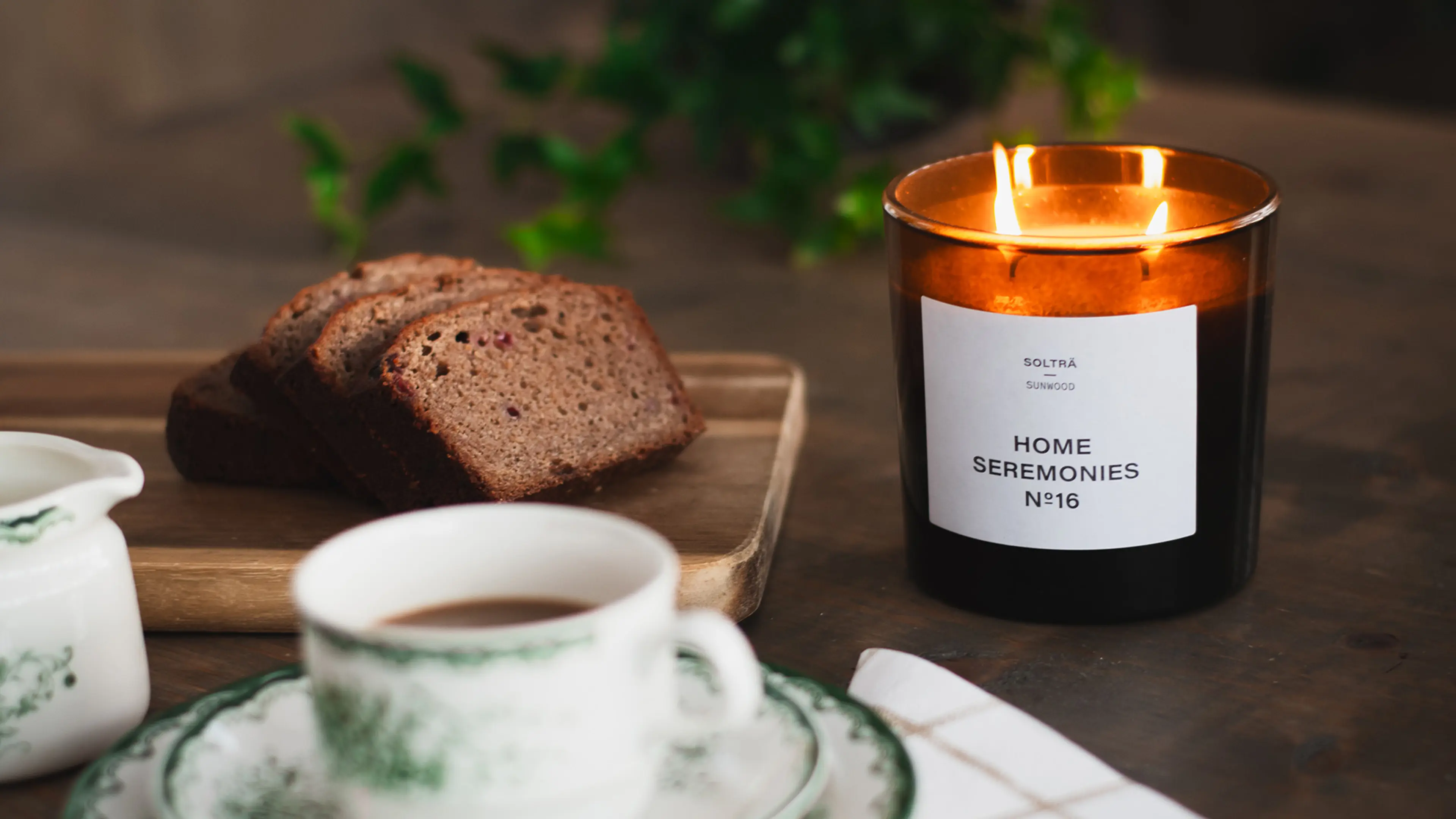 Doftljus från Home Seremonies på ett dukat mörk träbord med en kaffekopp och några bitar mjuk pepparkaka