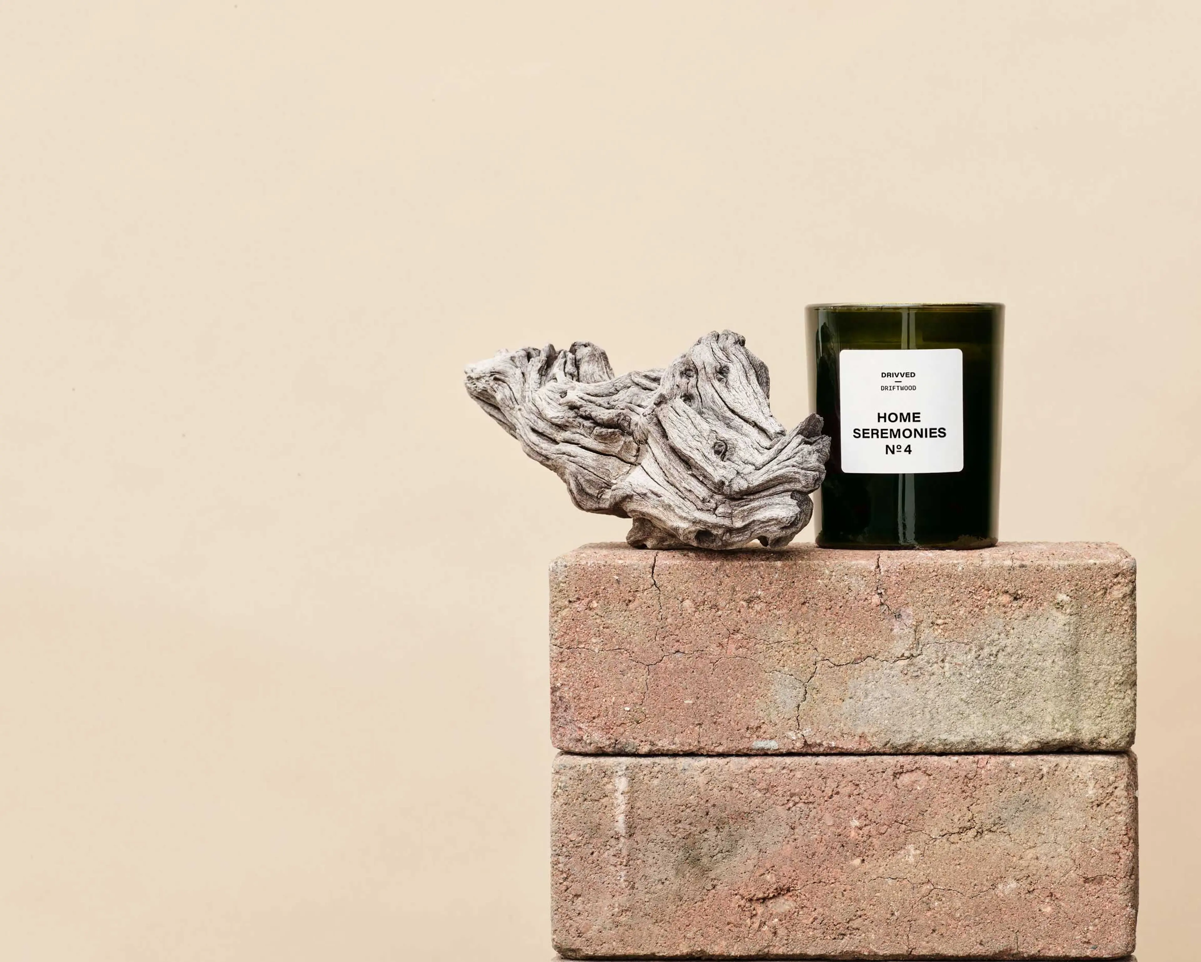 Doftljus i mörkt glas med etikett, placerat på två staplade tegelstenar tillsammans med en bit drivved.