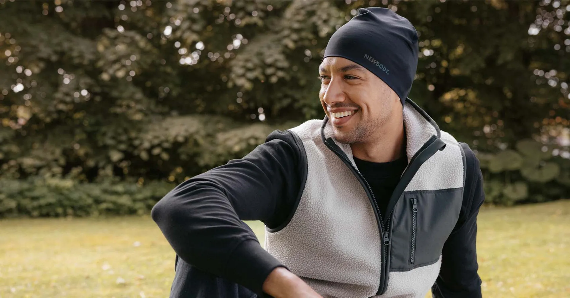 Man i mjuk beige pile vest med gröna detaljer, han sitter på en gräsmatta