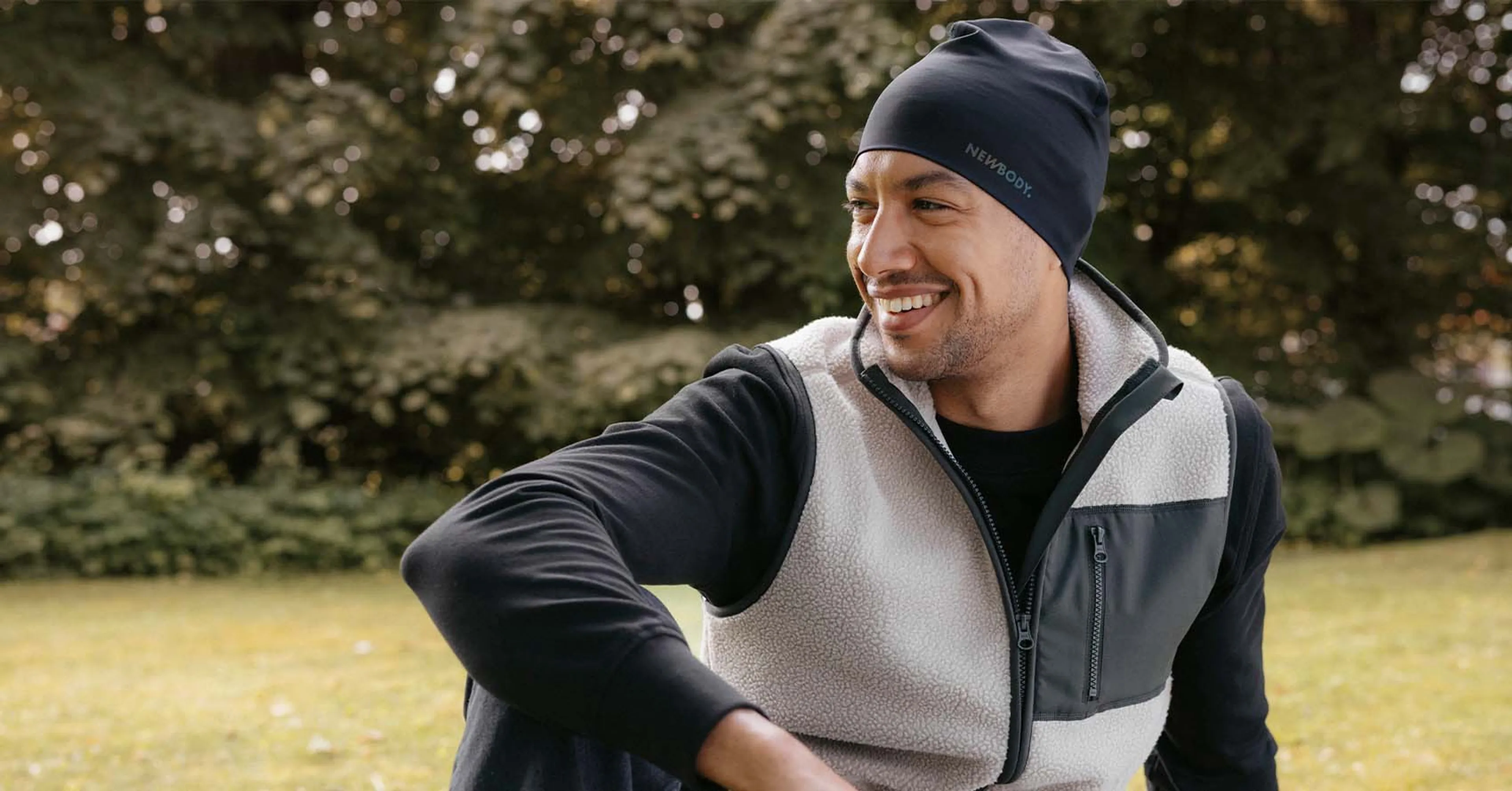 Man i mjuk beige pile vest med gröna detaljer, han sitter på en gräsmatta