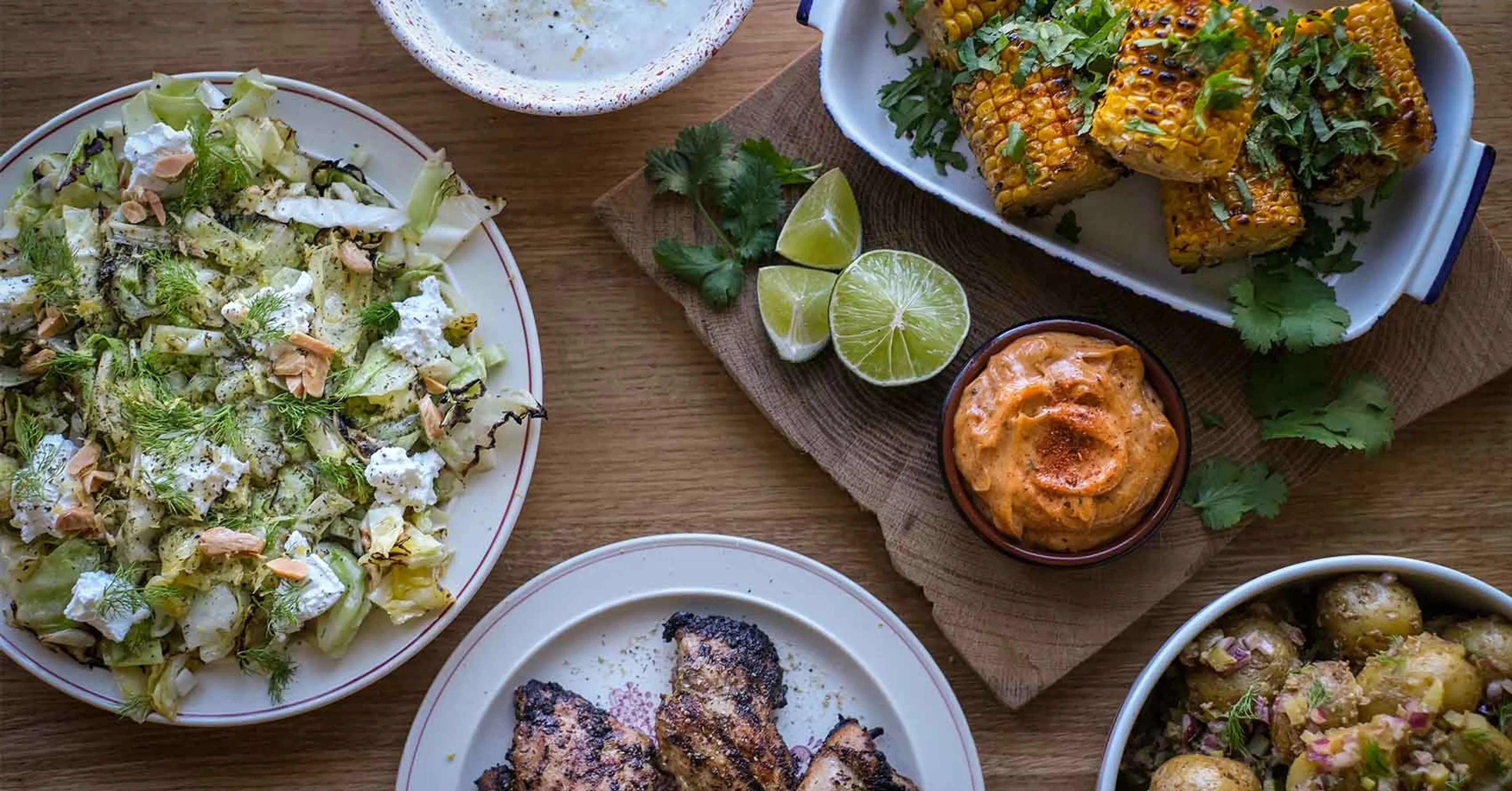 Grillade majskolvar med färsk koriander, limeklyftor och en krämig rödsås bredvid grillade köttbitar och en fräsch sallad med nötter och ost. En variation av smaker med både grönsaker och protein