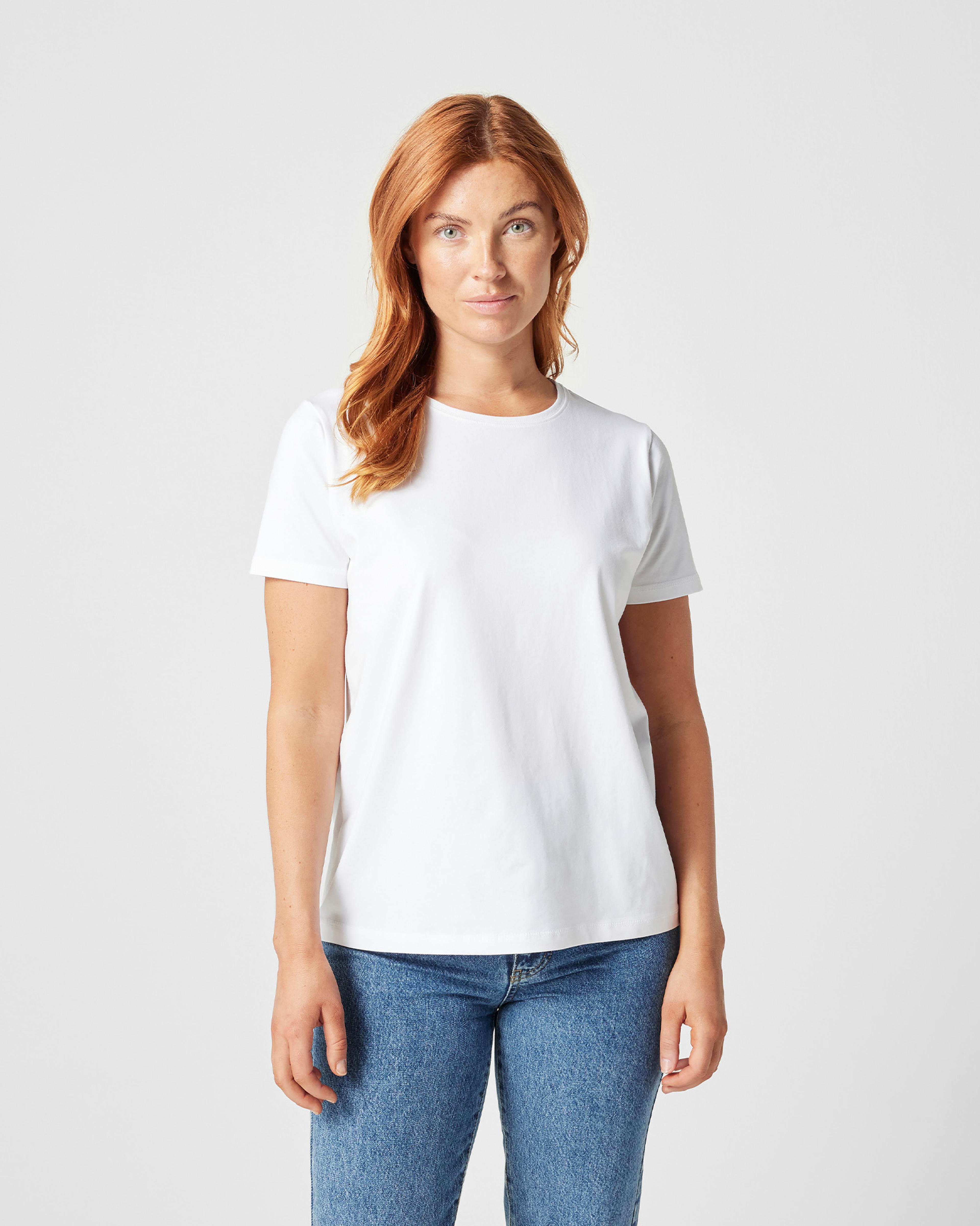 En enkel vit t-shirt med rund halsringning och korta ärmar, modellerad av en kvinna. T-shirten är mjuk och har en klassisk, rak passform.