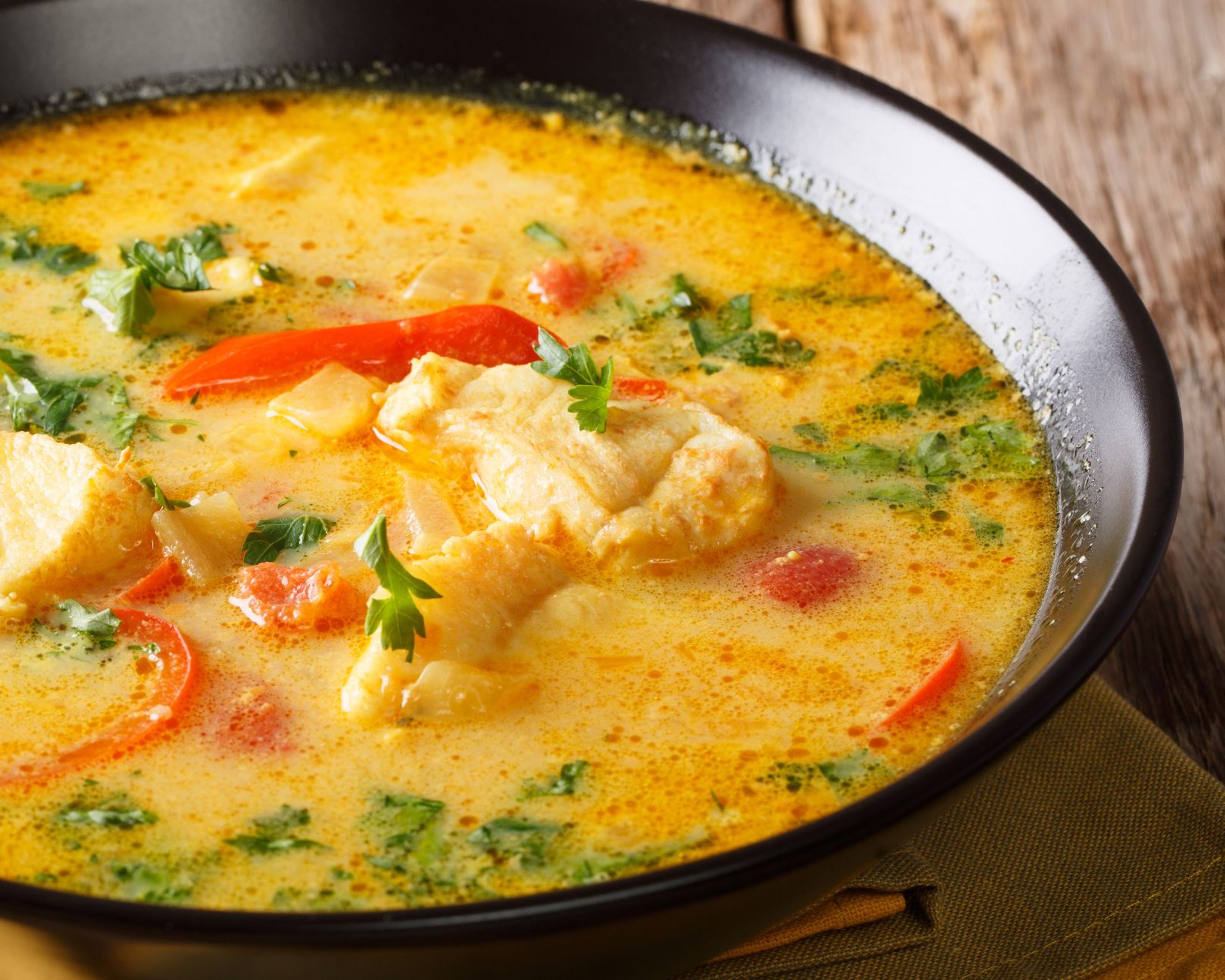 Krämig fisksoppa med saffran, röda paprikabitar och färsk persilja i en svart skål. Sopppan har en varm, gyllene färg med bitar av vit fisk.