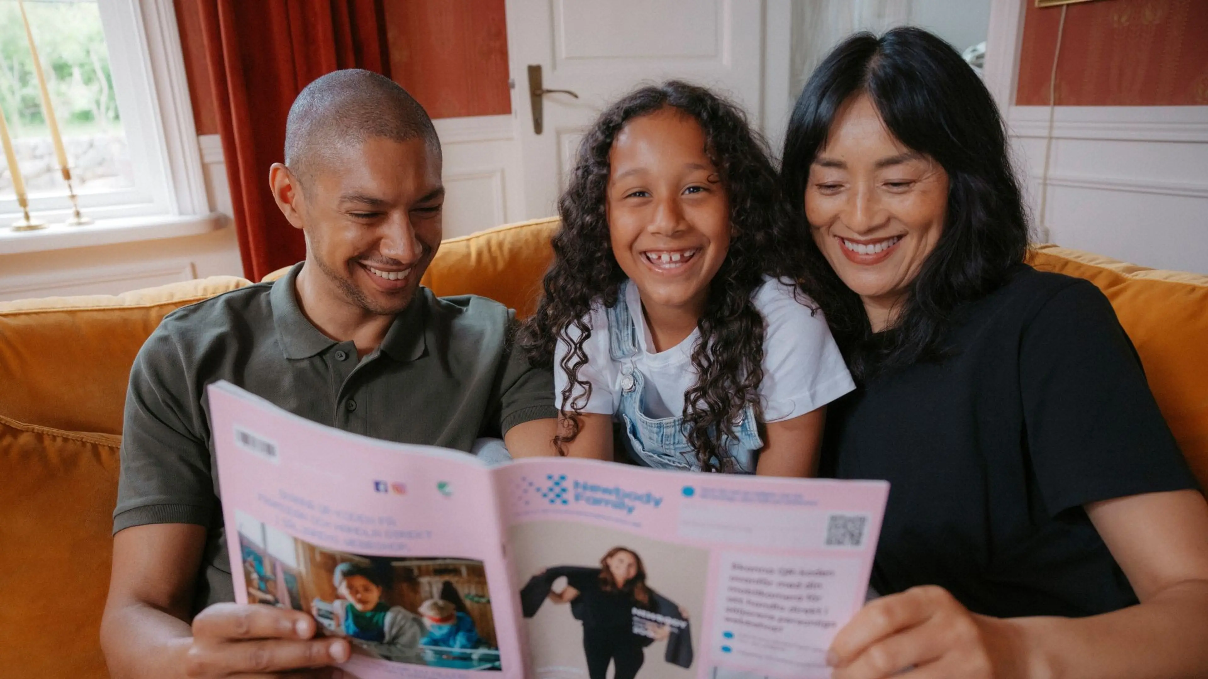 Mamma, pappa och dotter sitter i soffan och kollar i en Newbody katalog
