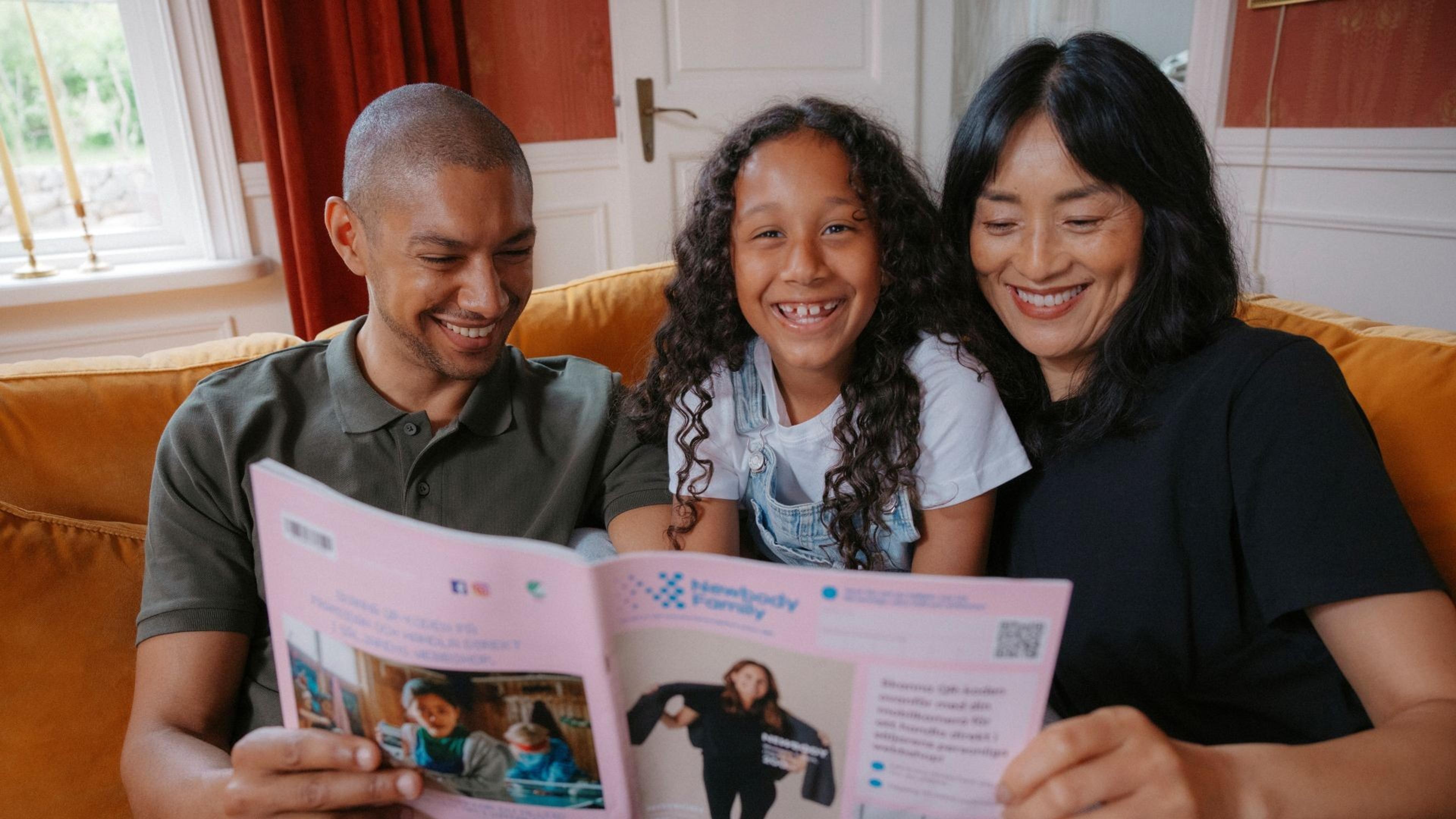 Mamma, pappa och dotter sitter i soffan och kollar i en Newbody katalog