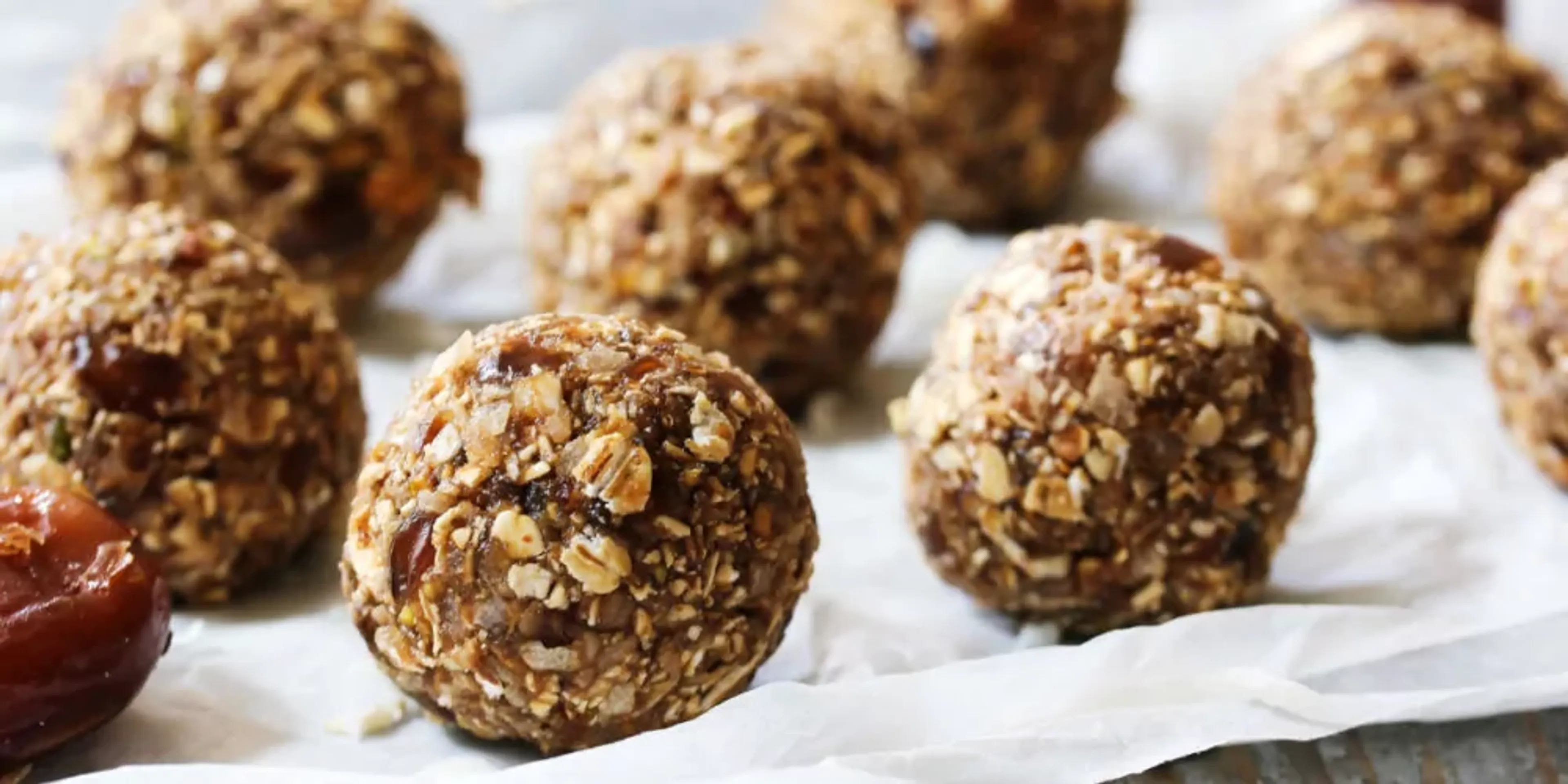 Runda energibollar gjorda på havre och torkad frukt, rullade till perfekta bollar. Flera bollar ligger på ett bakpapper i en närbild.