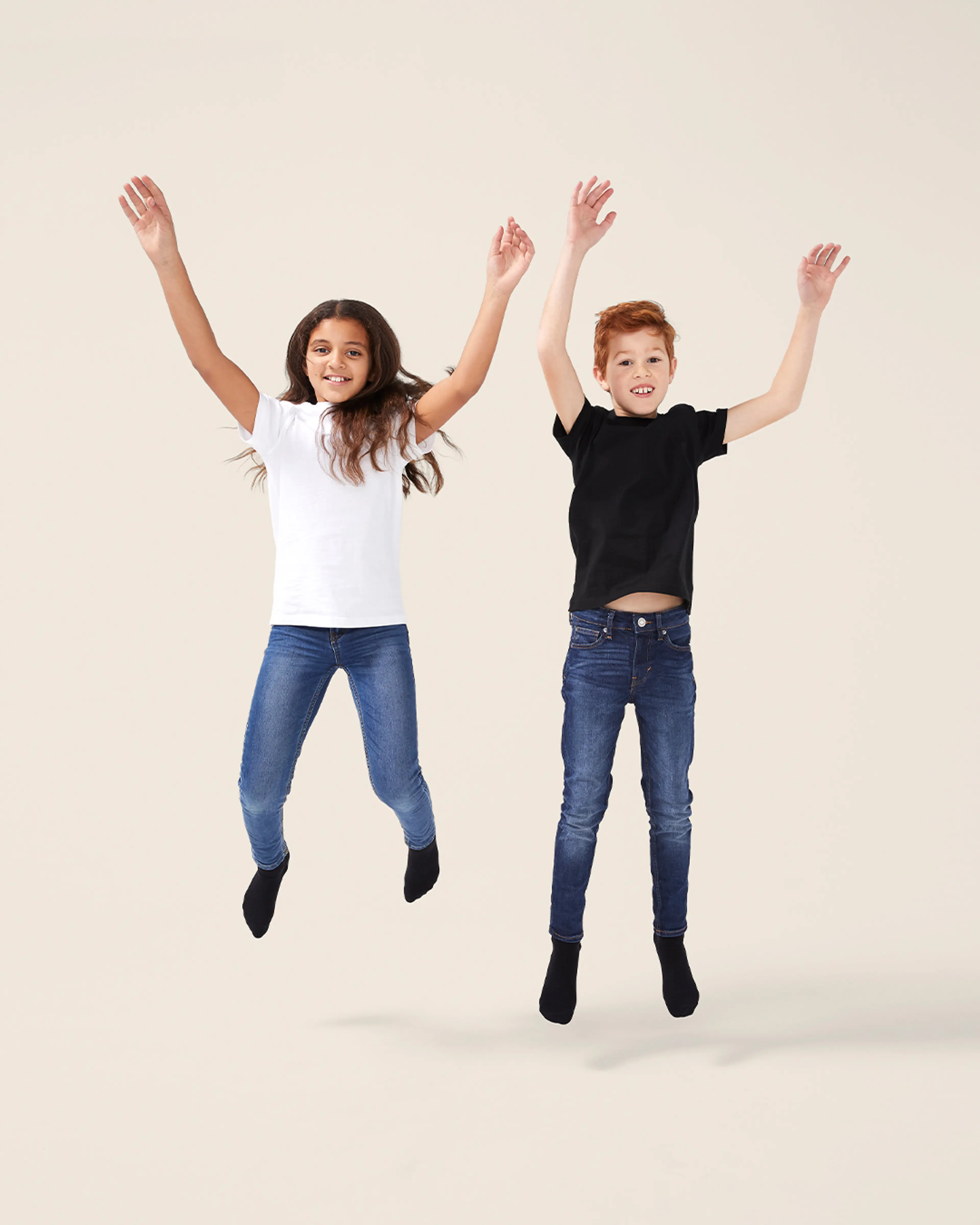 Två barn hoppar glatt och bär enkla, enfärgade t-shirts i svart och vitt tillsammans med mörkblå jeans och svarta strumpor.