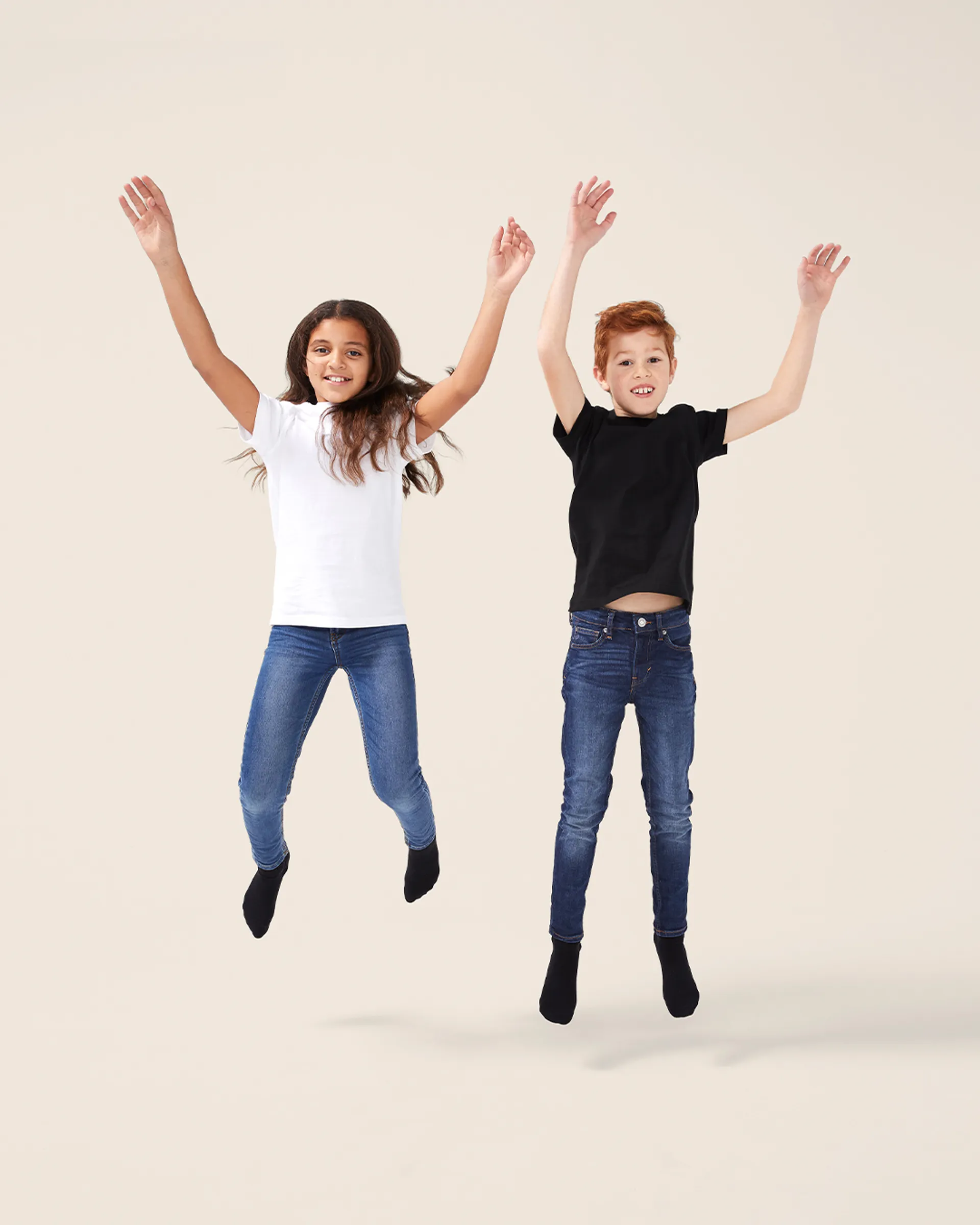 Två barn hoppar glatt och bär enkla, enfärgade t-shirts i svart och vitt tillsammans med mörkblå jeans och svarta strumpor.