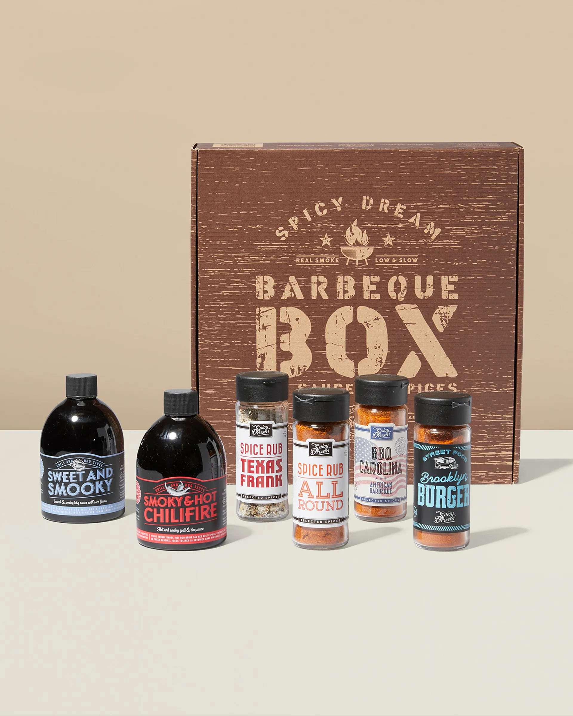 En barbeque-box med två flaskor grillsåser och fyra burkar kryddblandningar i olika smaker, för att ge maten extra sting och karaktär. Boxen har en rustik trädesign med texten "Barbeque Box".