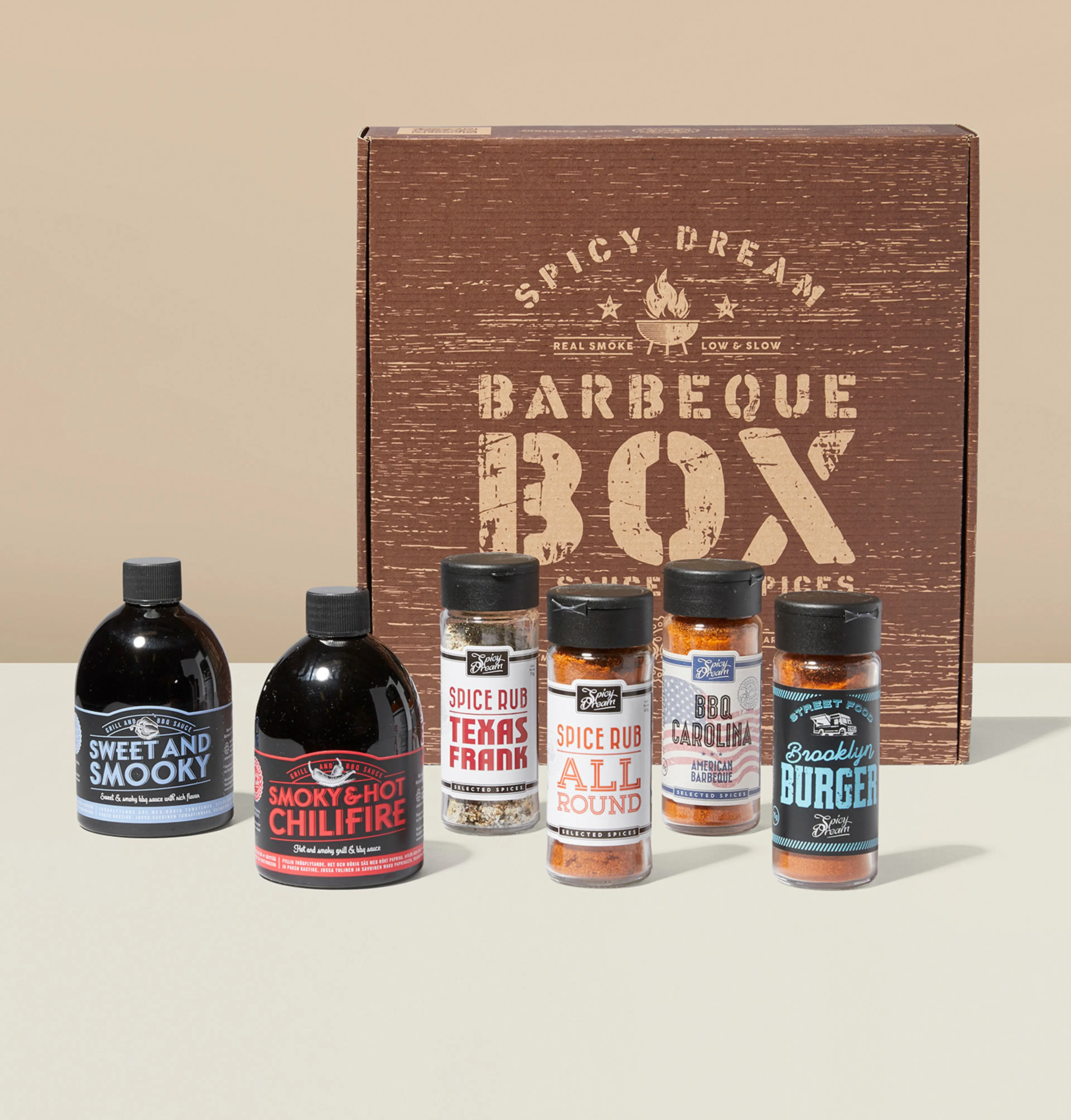 En barbeque-box med två flaskor grillsåser och fyra burkar kryddblandningar i olika smaker, för att ge maten extra sting och karaktär. Boxen har en rustik trädesign med texten "Barbeque Box".