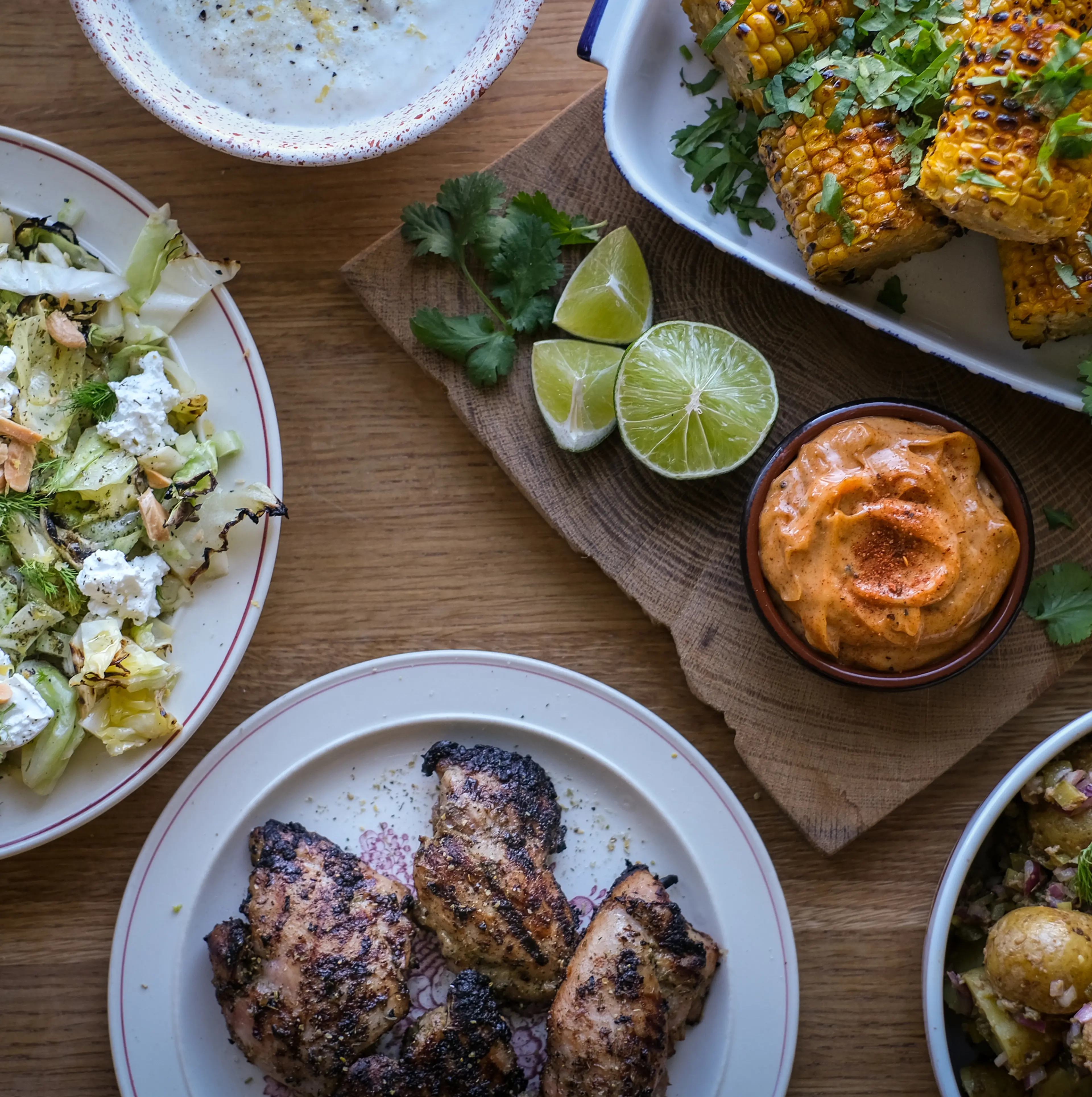 Grillad majskolv med färsk koriander, grillade kycklingbitar och en fräsch sallad med nötter och örter. Limeklyftor och två olika dippsåser kompletterar måltiden.