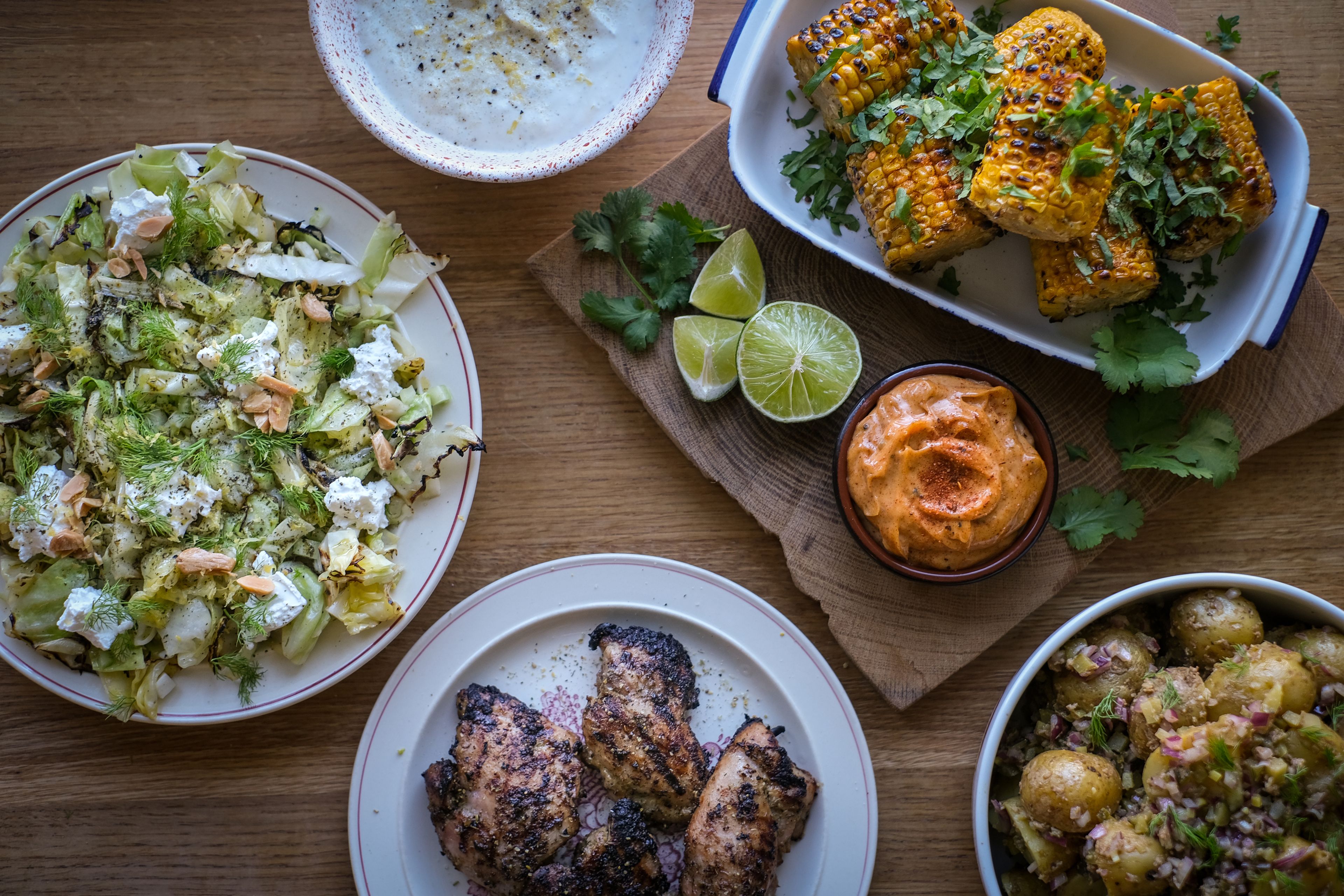Grillad majskolv med färsk koriander, grillade kycklingbitar och en fräsch sallad med nötter och örter. Limeklyftor och två olika dippsåser kompletterar måltiden.