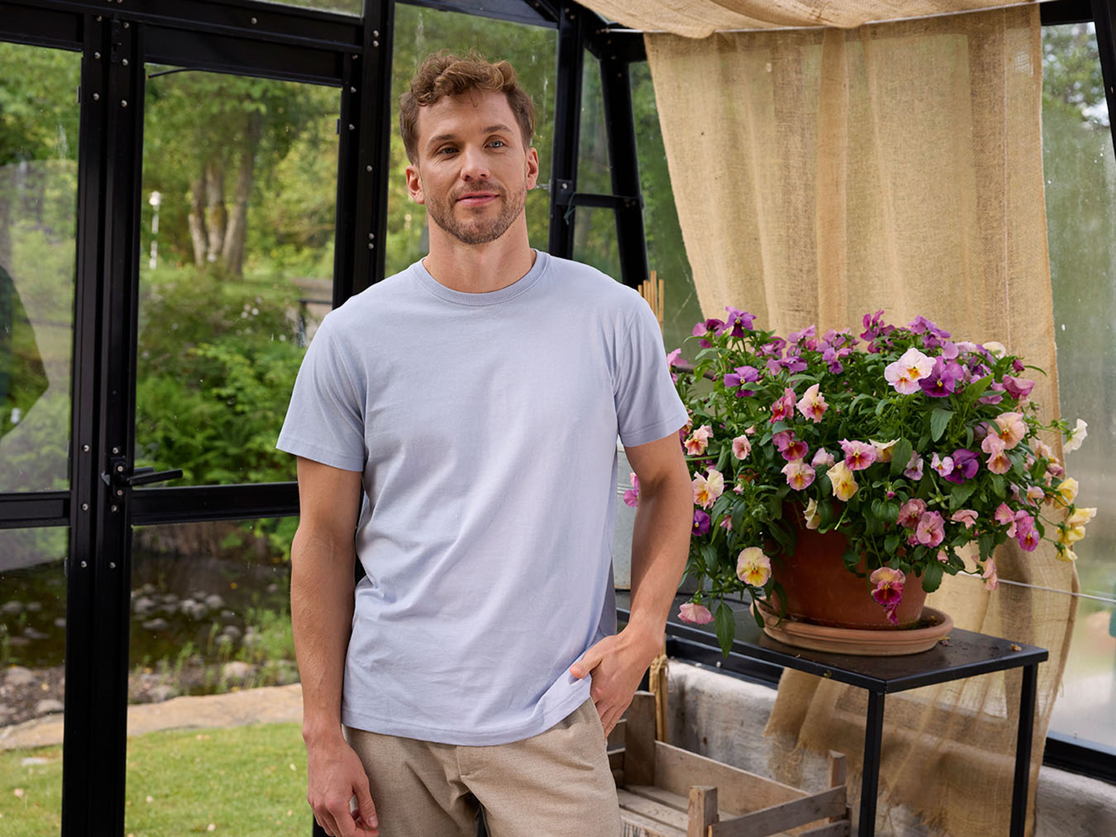 Man i ljusblå men's tshirt, ståendes i ett växthus