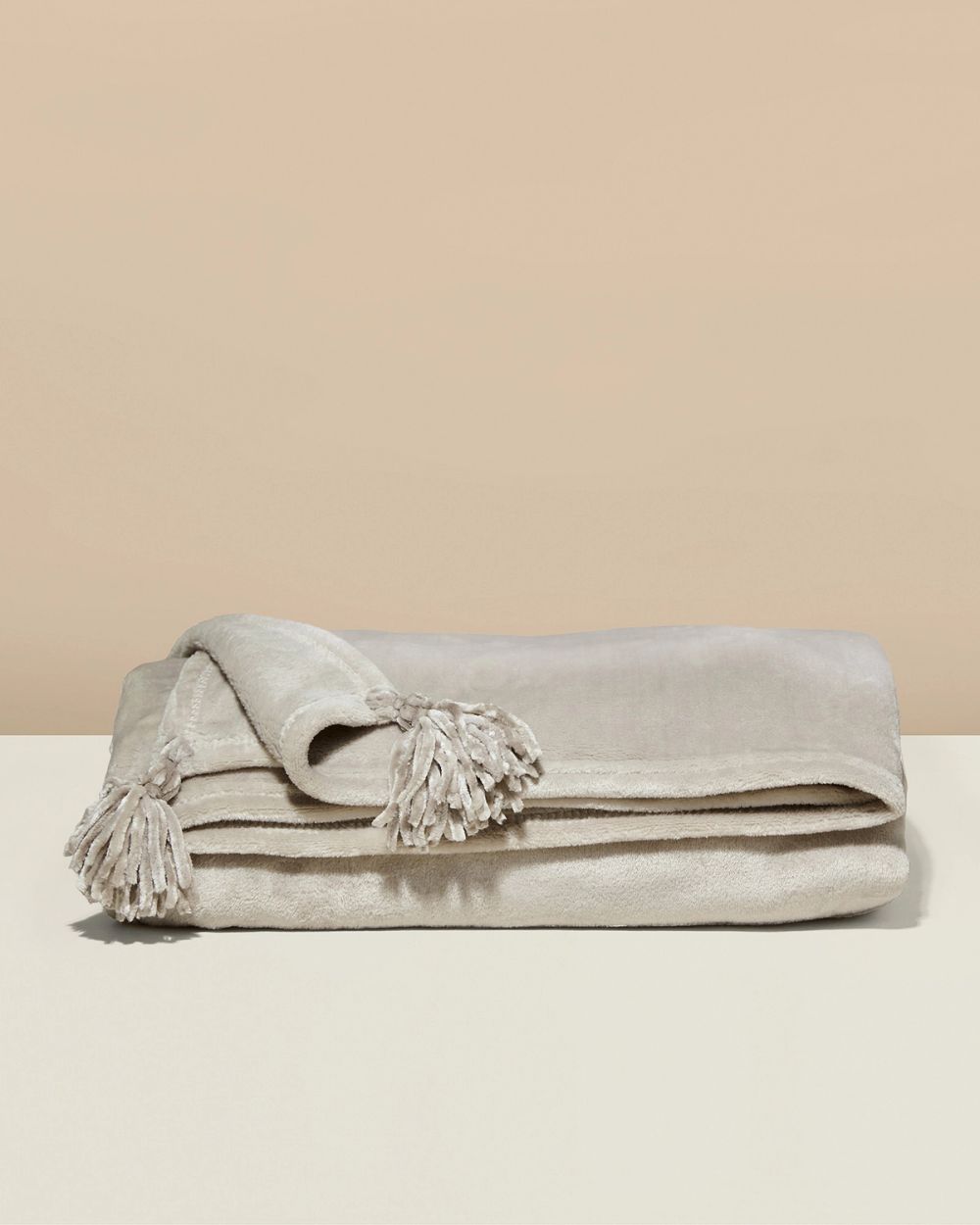 Mjuk och varm fleecepläd i beige med dekorativa tofsar i hörnen. Perfekt för mysiga stunder hemma eller som en extra värmekälla.
