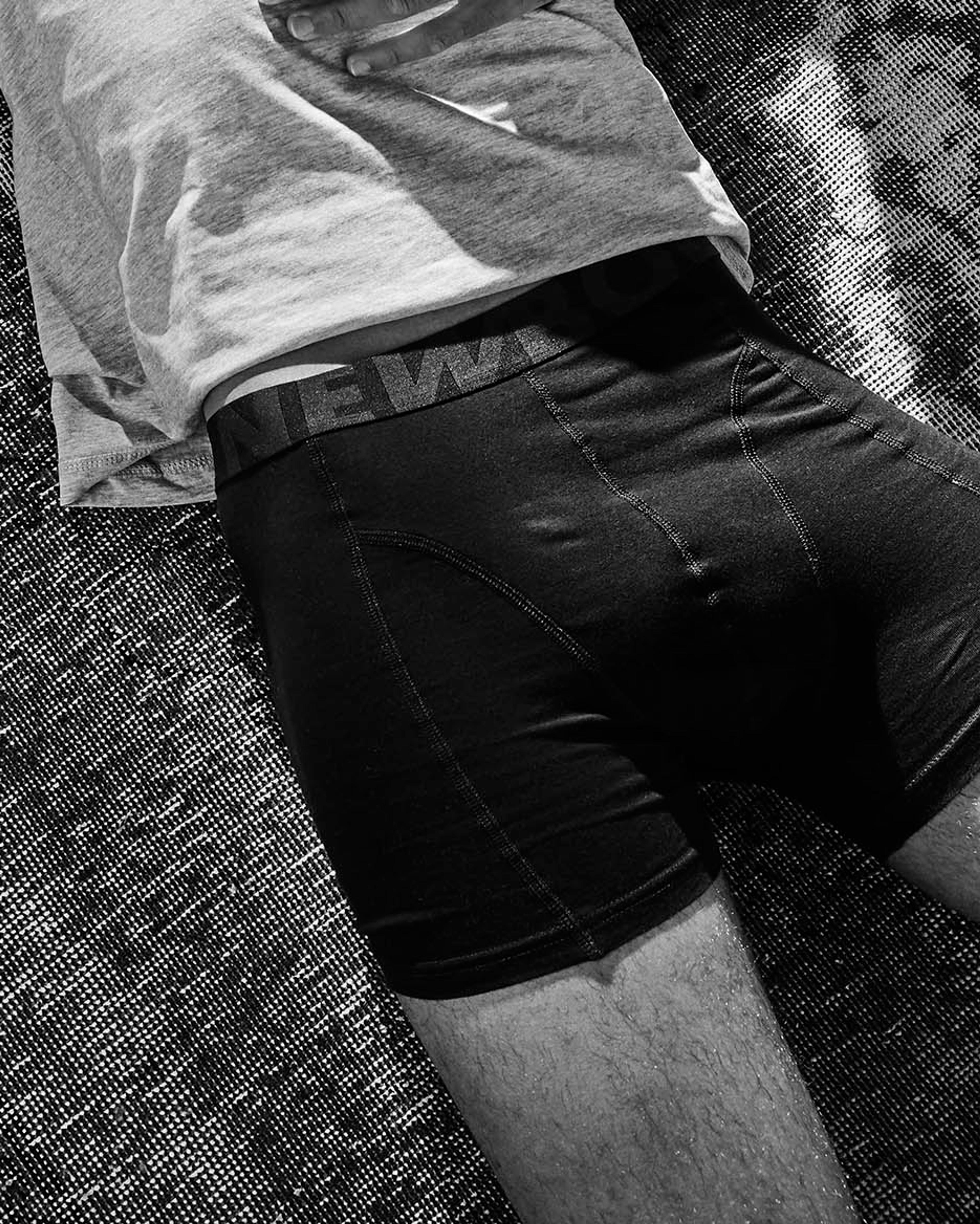 En person ligger avslappnat på en matta med hörlurar på och en t-shirt tillsammans med svarta, åtsittande boxer-kalsonger. Intill ligger en hög vinylskivor med en skiva överst.